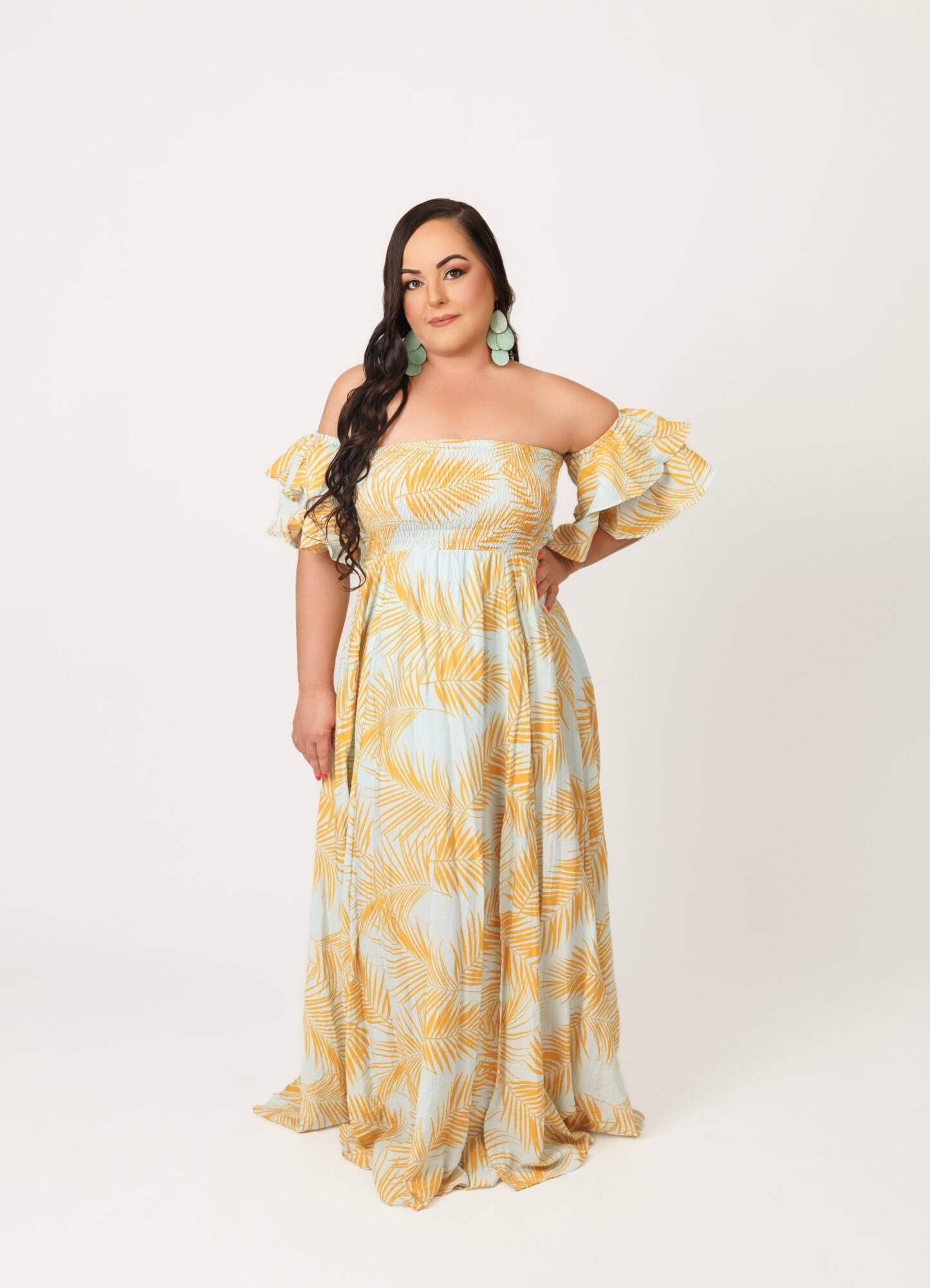 Woman in a yellow and white off-shoulder dress with ruffled sleeves, standing against a plain white background.