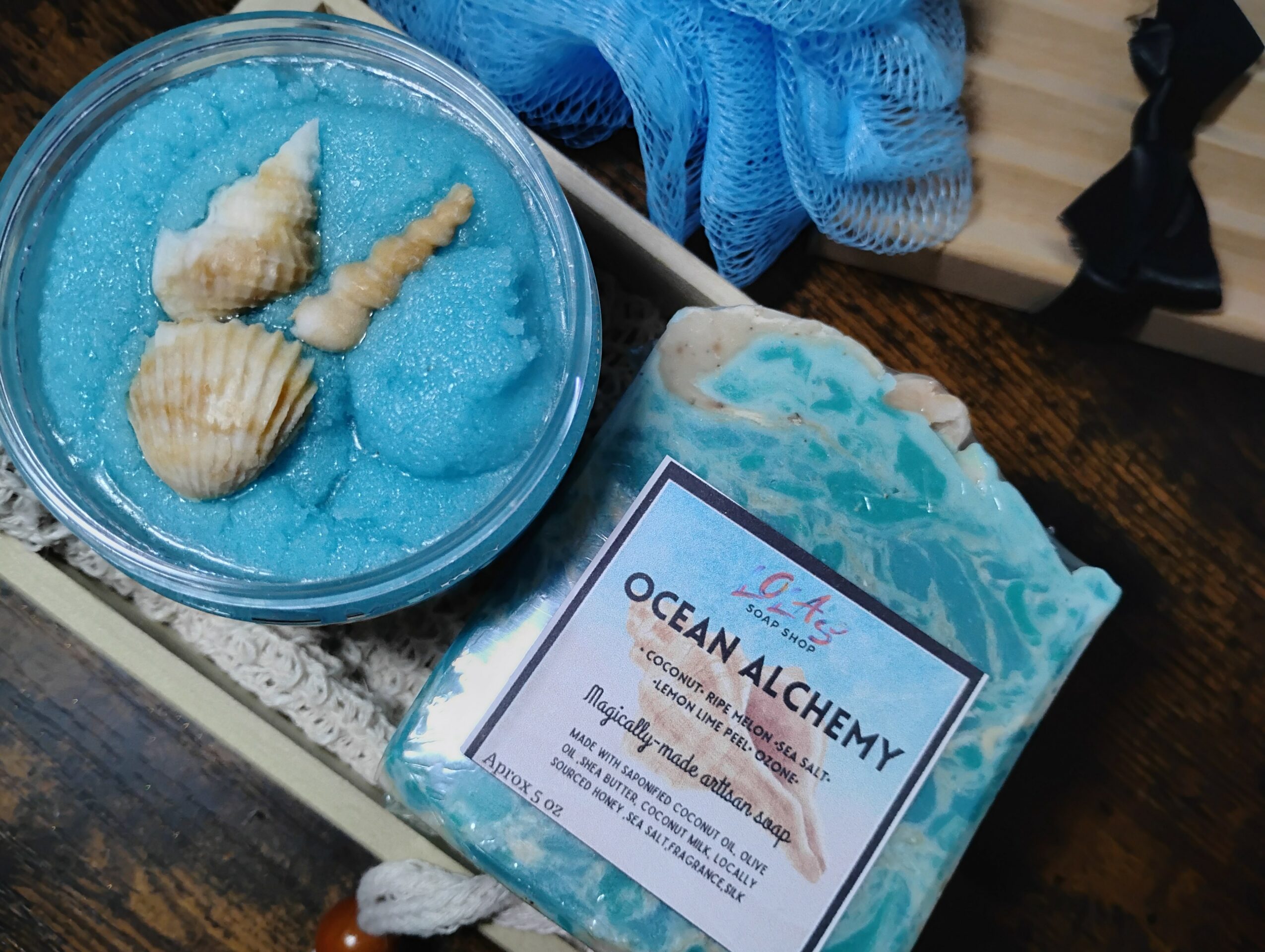 A shell-shaped soap and a blue bath bomb labeled 'Ocean Alchemy' on a wooden surface.