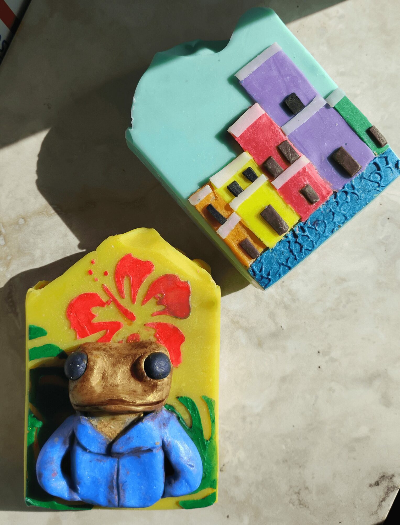 Colorful foam block with a frog figure wearing a blue hoodie, and a cityscape with buildings, on a light surface.