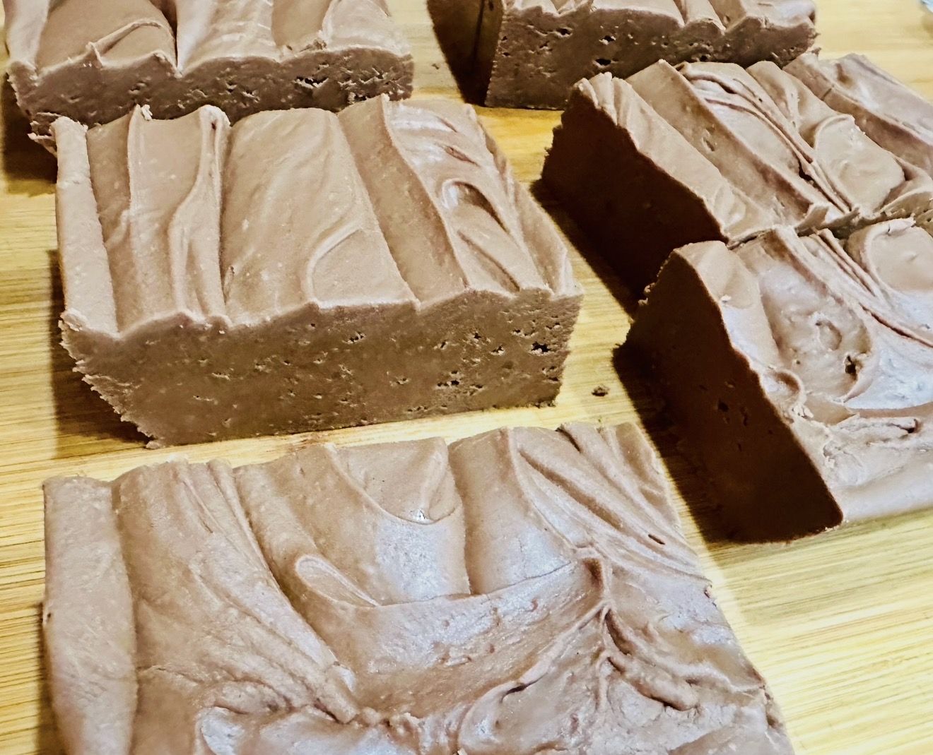 Four pieces of chocolate soap with swirled patterns on a wooden surface.