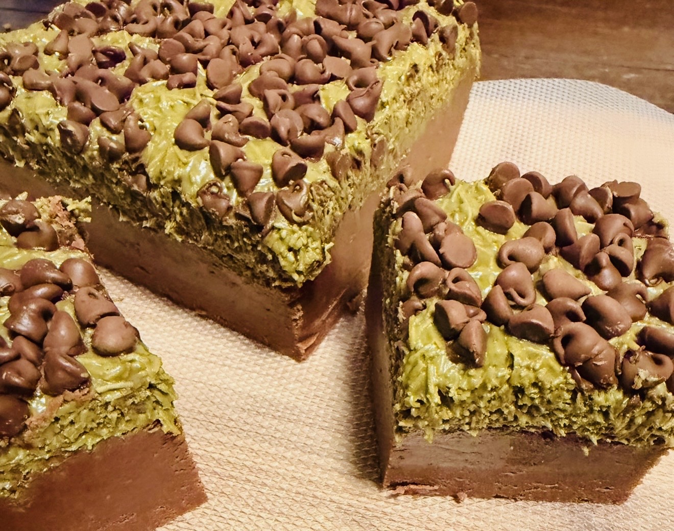 Three slices of layered cake with green and chocolate layers topped with chocolate chips on a white surface.