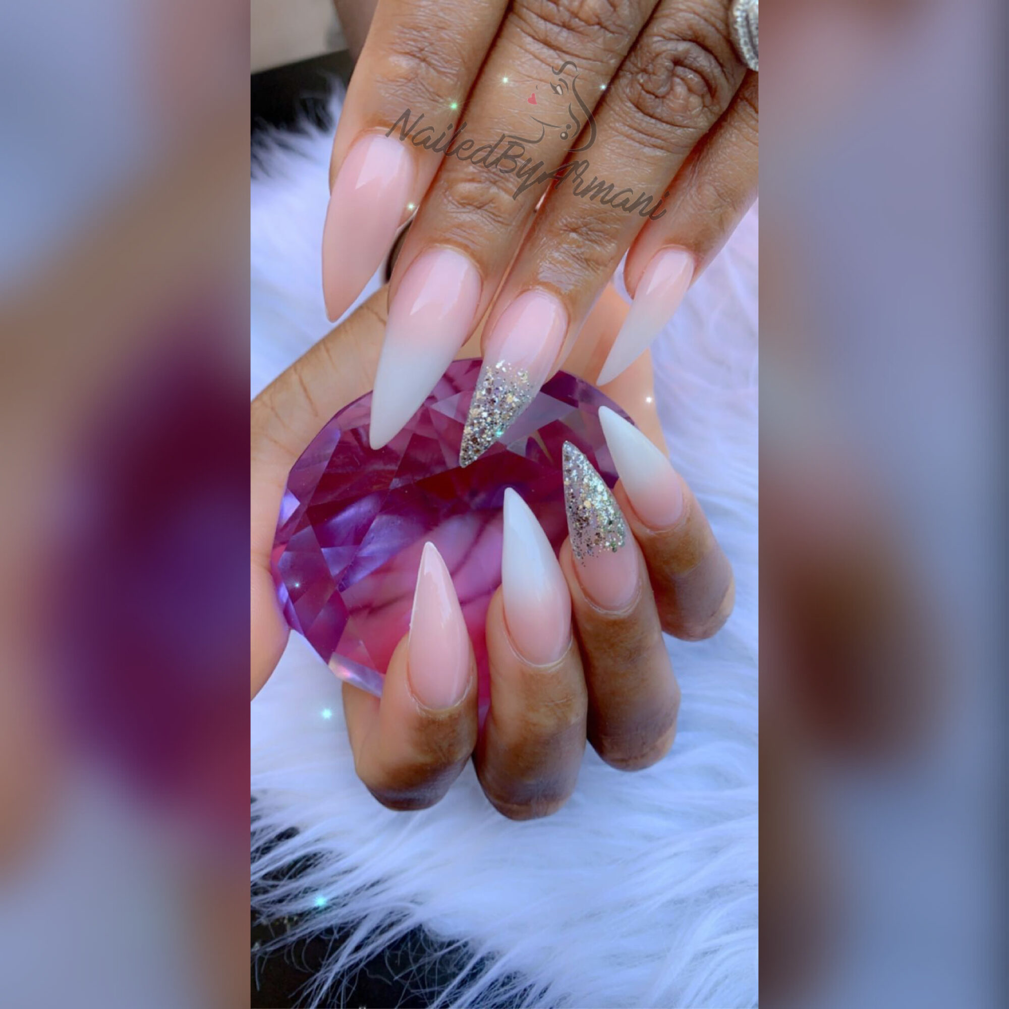 Close-up of a hand with long, almond-shaped nails, some with glitter, holding a purple gemstone, resting on white fur.