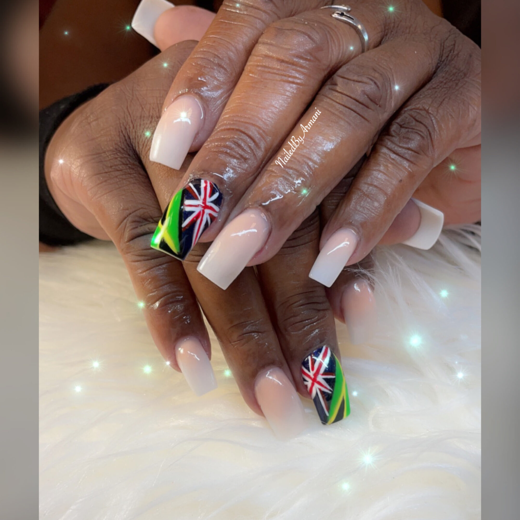 Close-up of hands with manicured nails, featuring Union Jack and South African flag designs on accent nails, resting on a soft surface.