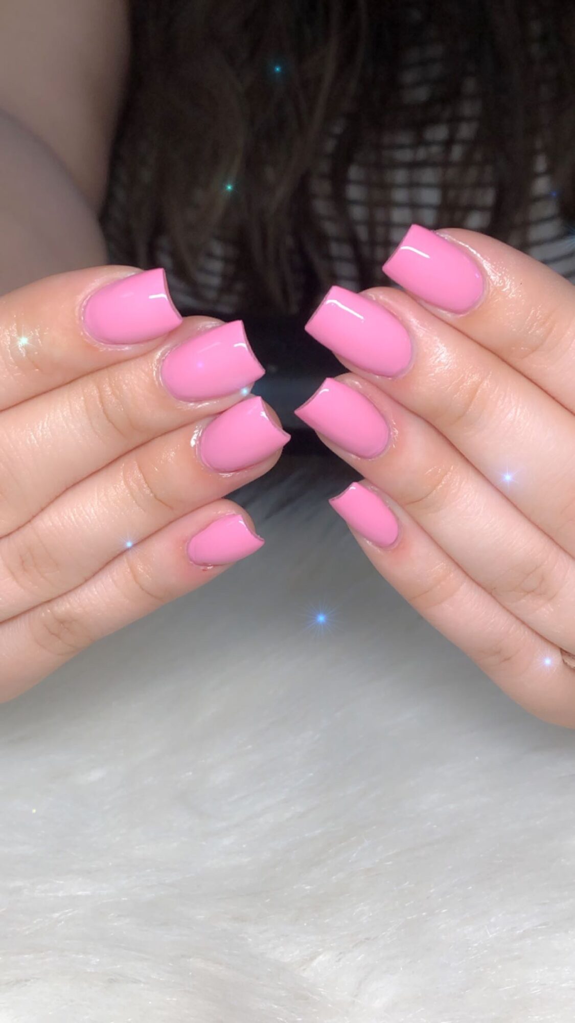 Person with pink nail polish holding a black object, background shows part of a striped shirt and long hair.