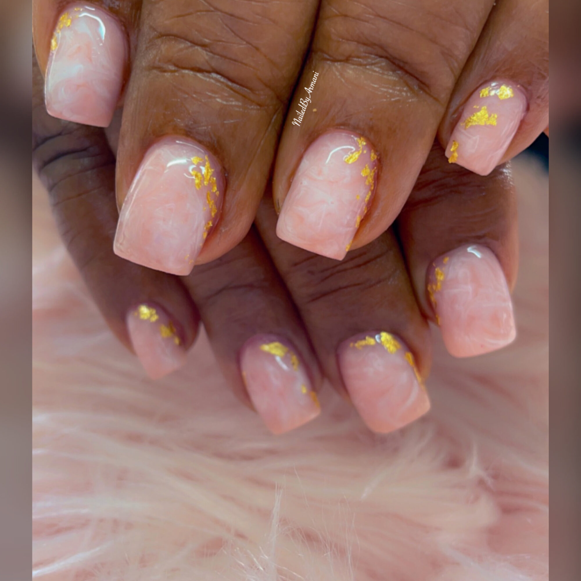 Close-up of manicured nails with light pink polish and yellow accents, resting on a soft pink surface.