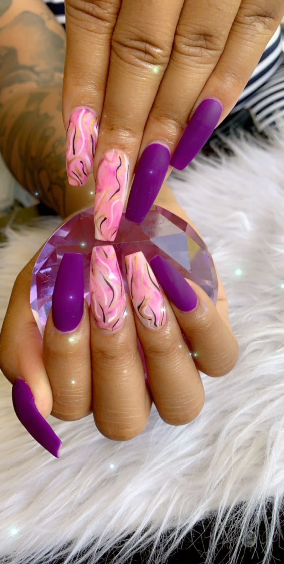 Close-up of hands with purple and marbled pink nails holding a faceted crystal ball on a white furry surface.
