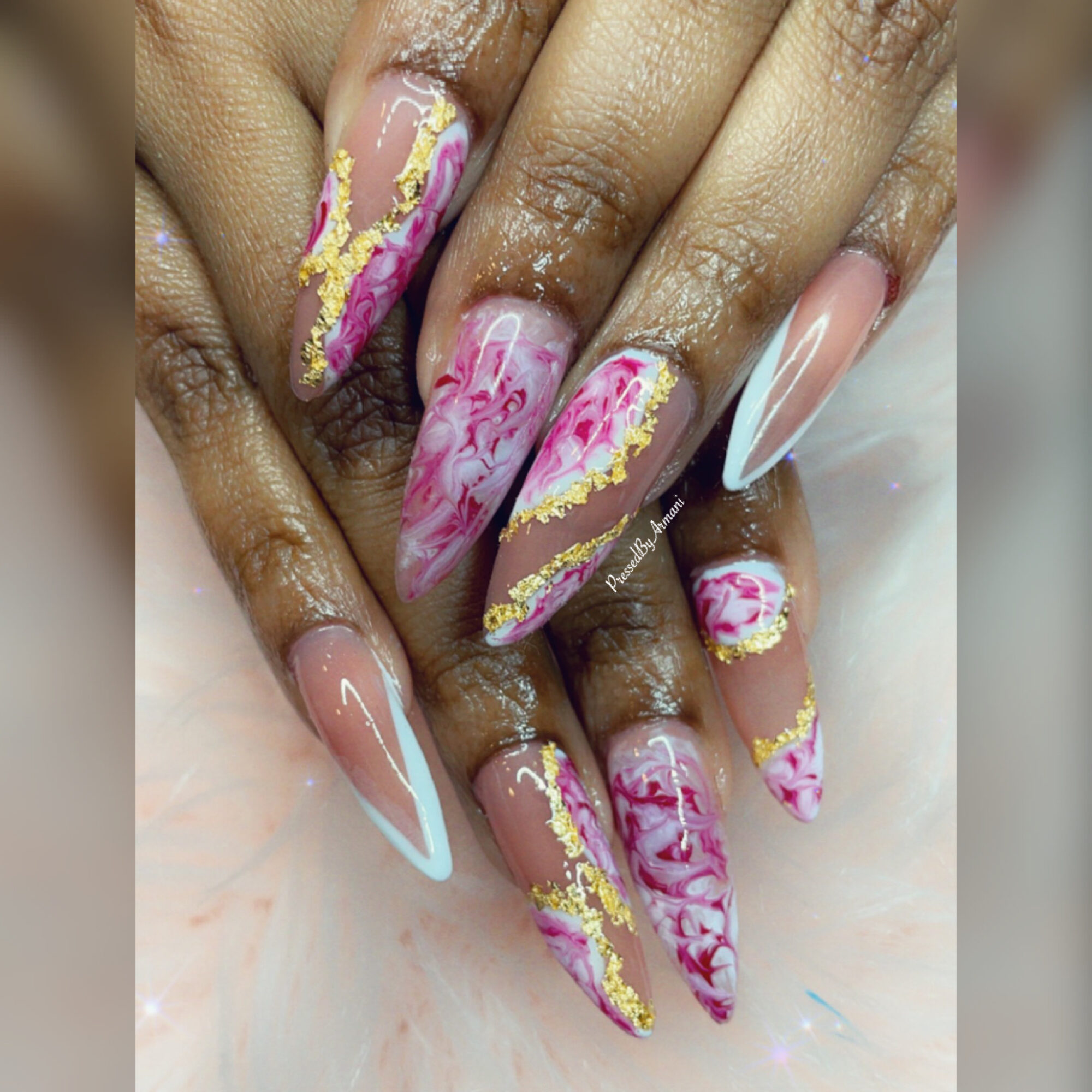 Close-up of decorated long nails with pink, white, and gold marble and swirl designs, some with white tips.