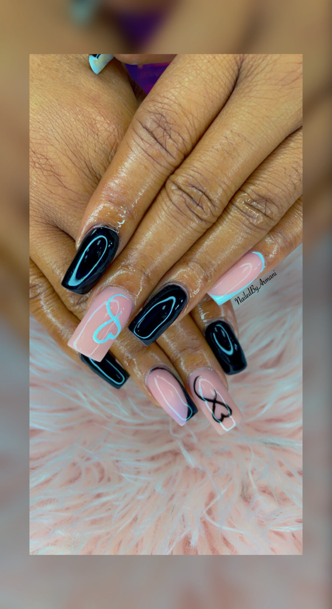 Close-up of hands with decorated nails, featuring black, pink, and blue designs, resting on a pink furry surface.