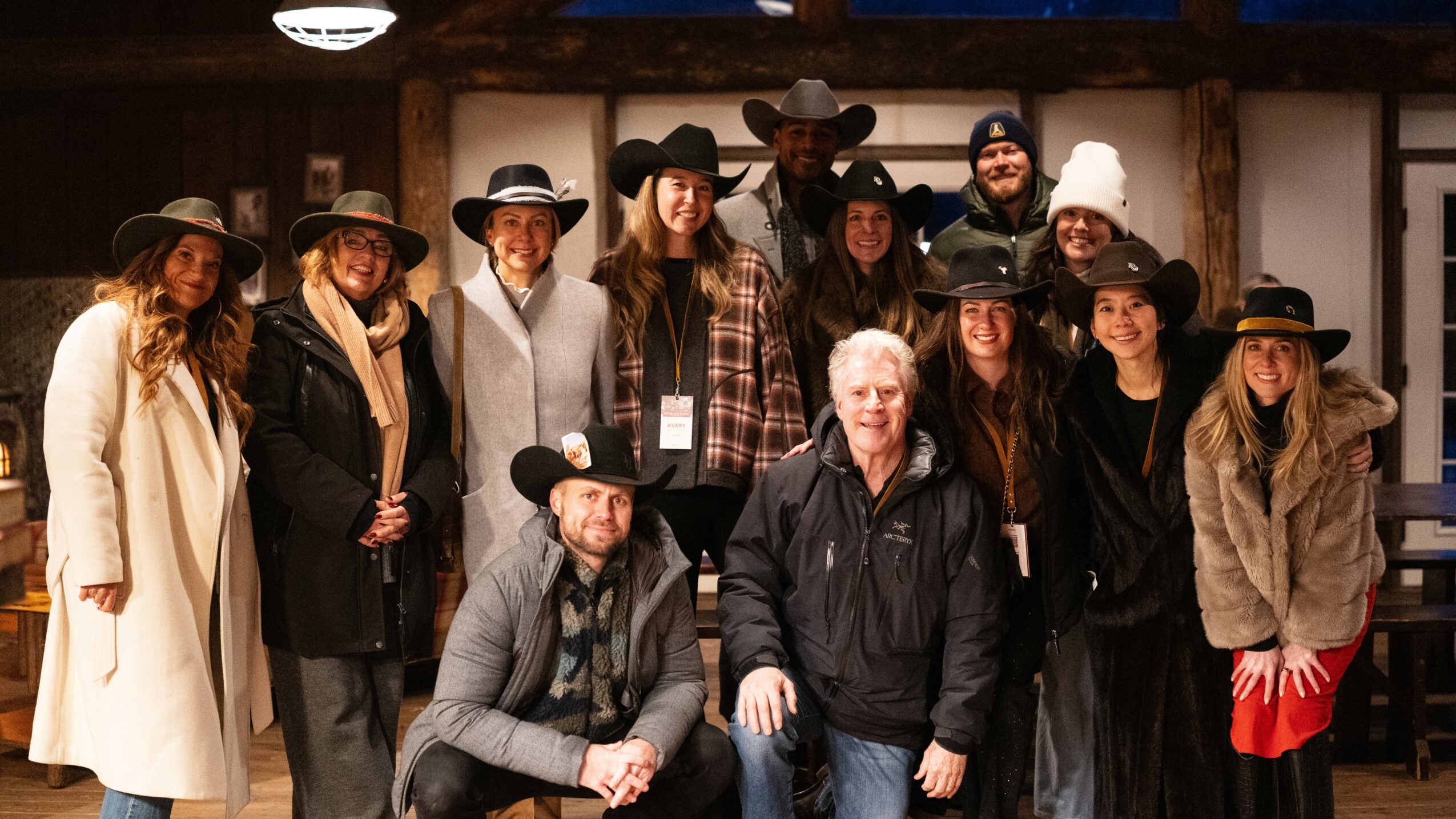 Group of people, some wearing hats, posing indoors with wooden beams in background.