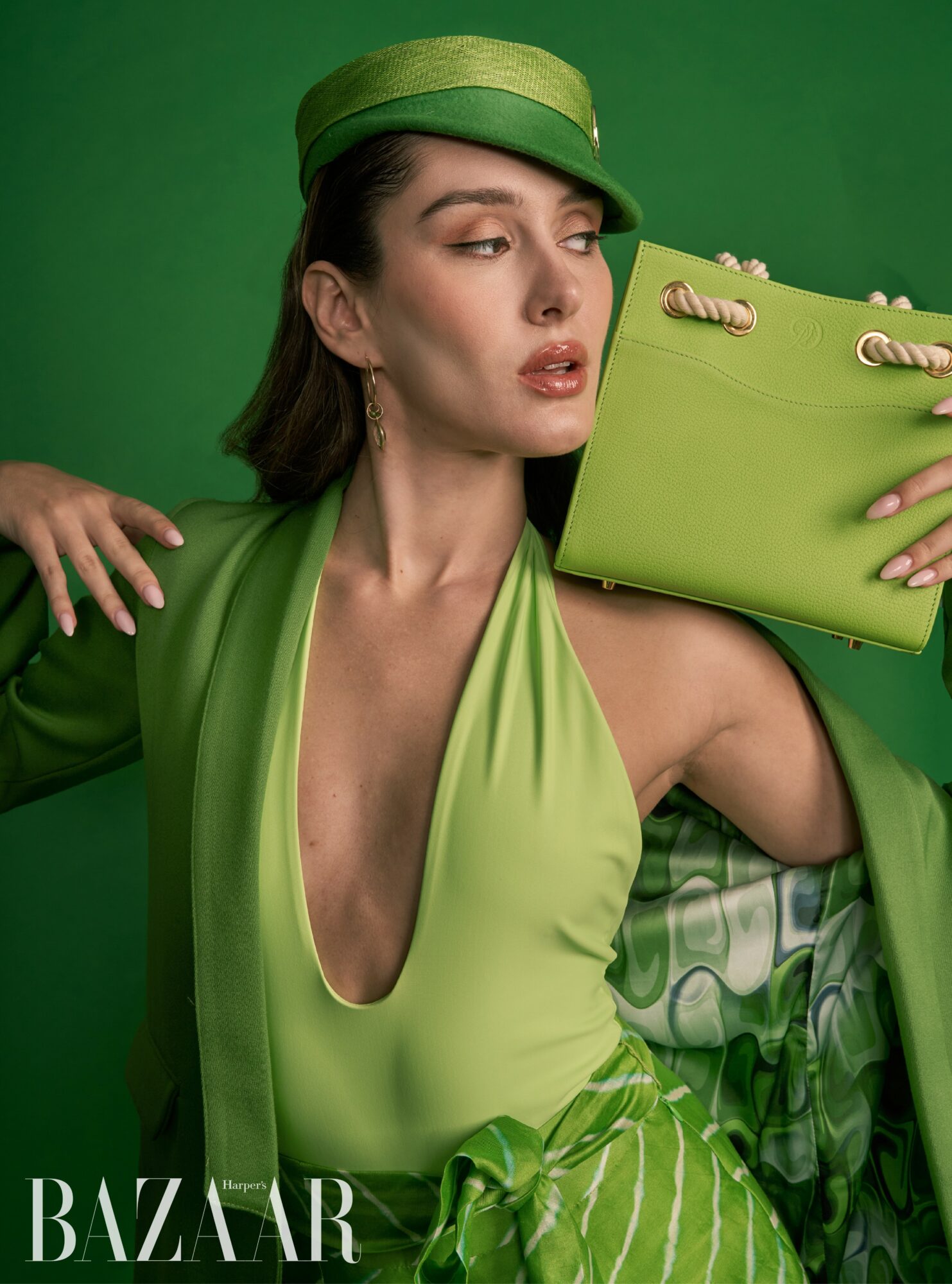 Woman in green outfit holding a matching green handbag against a green background.