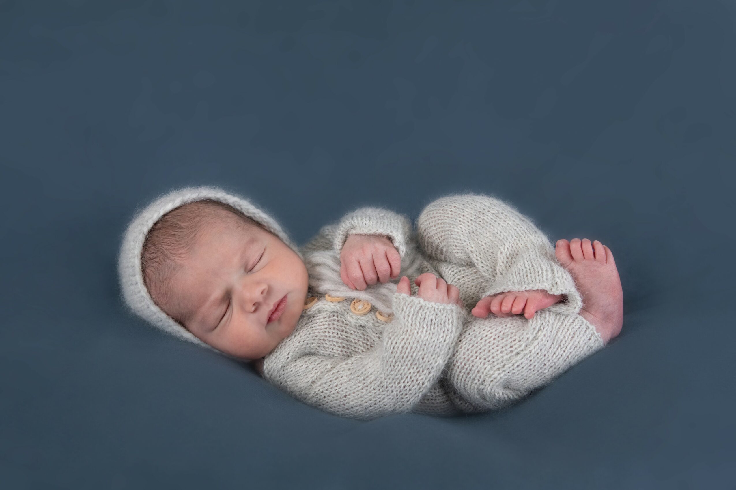 Sleeping baby in knitted outfit and hat, lying on a dark blue surface.
