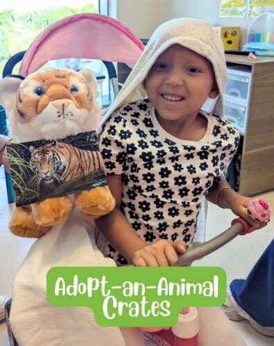 Child smiling with a towel on head, holding a pink toy, in a room with stuffed animals and furniture.