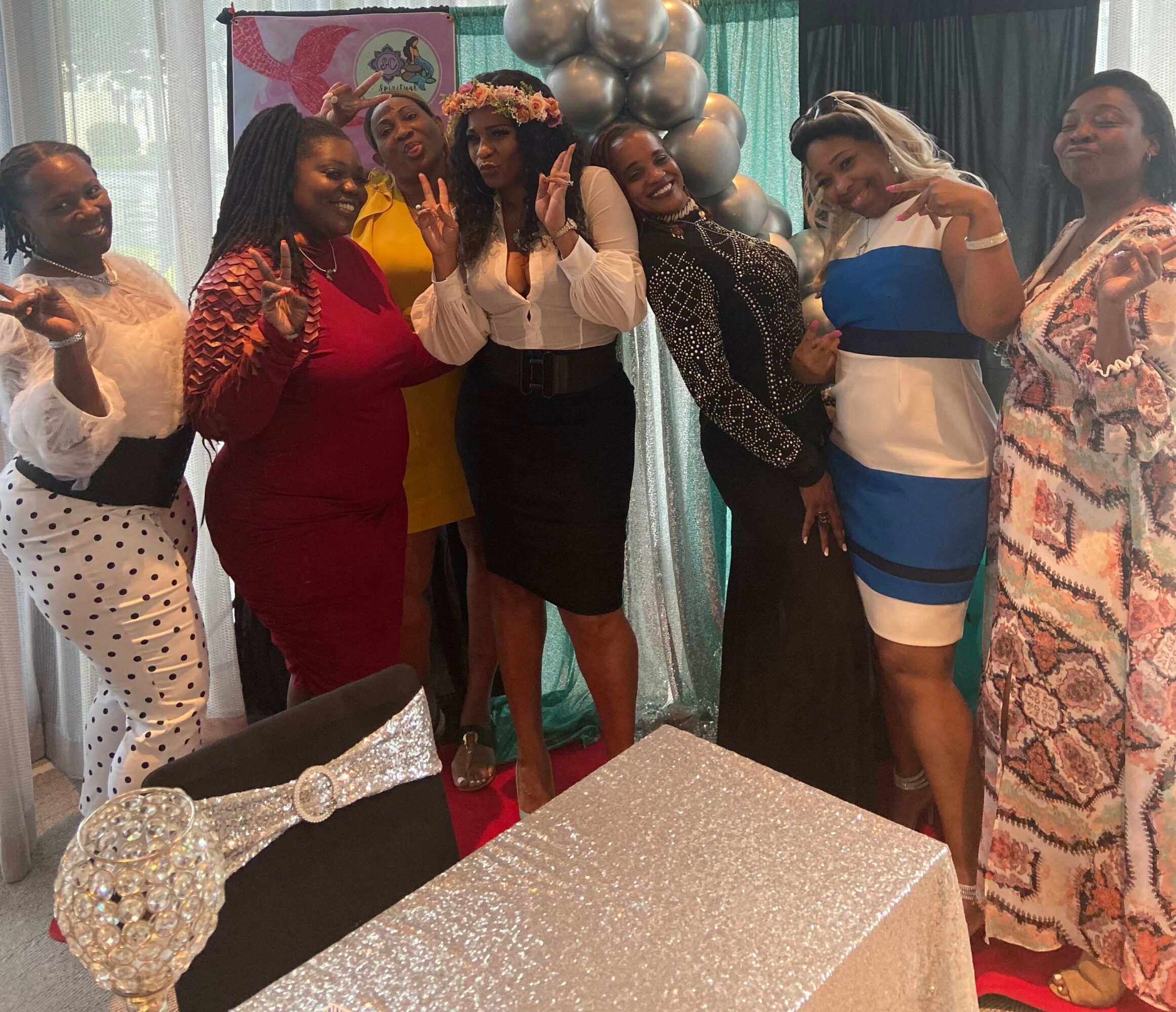 Group of women smiling and posing at a celebration, with balloons and decorations in the background.