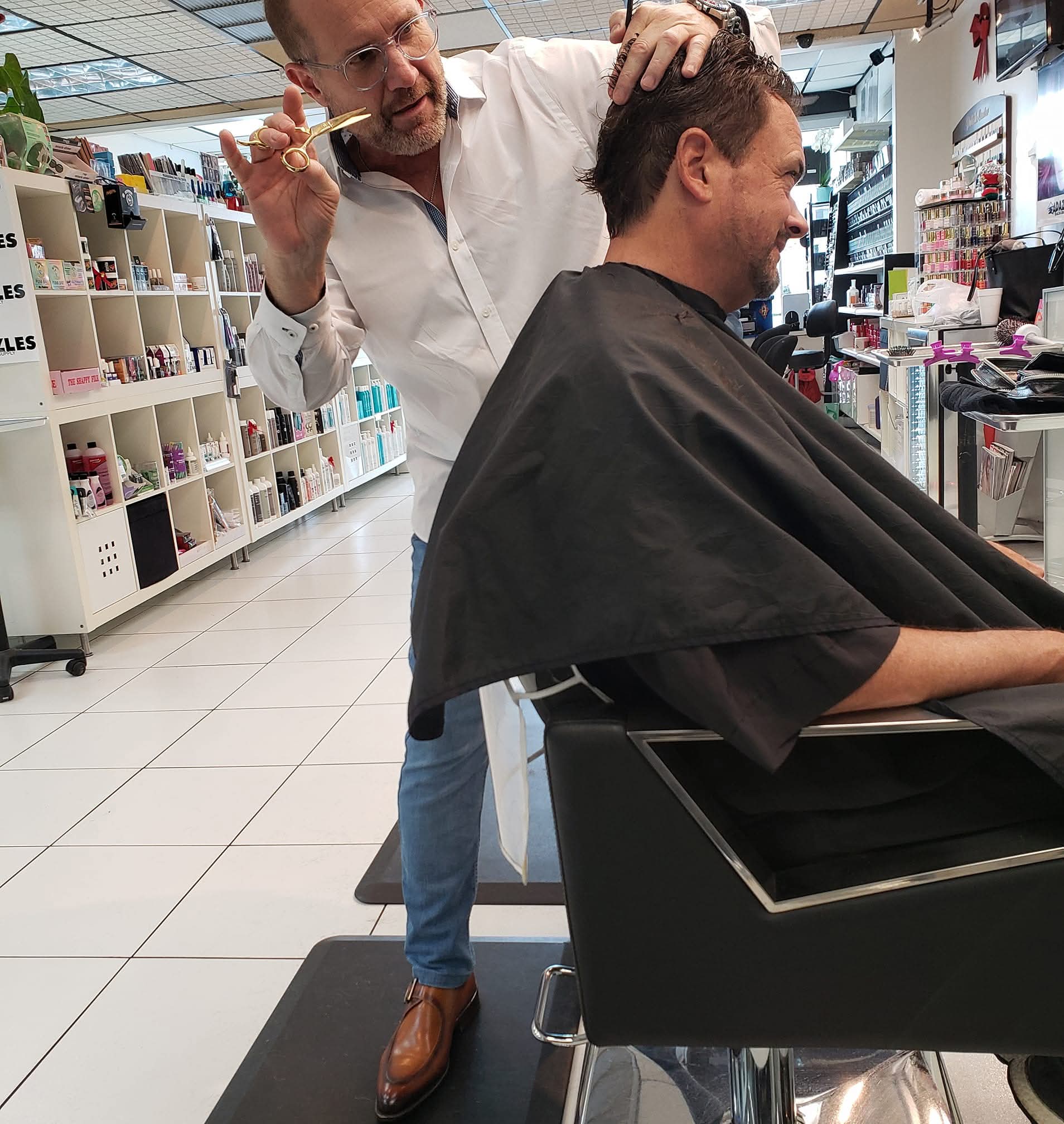 Barber cutting a man's hair in a store, shelves with products in the background.