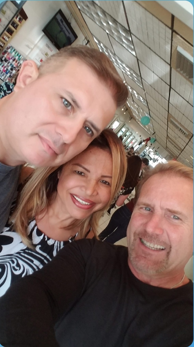 Three people smiling in an indoor setting, two men and one woman, close together for a selfie.
