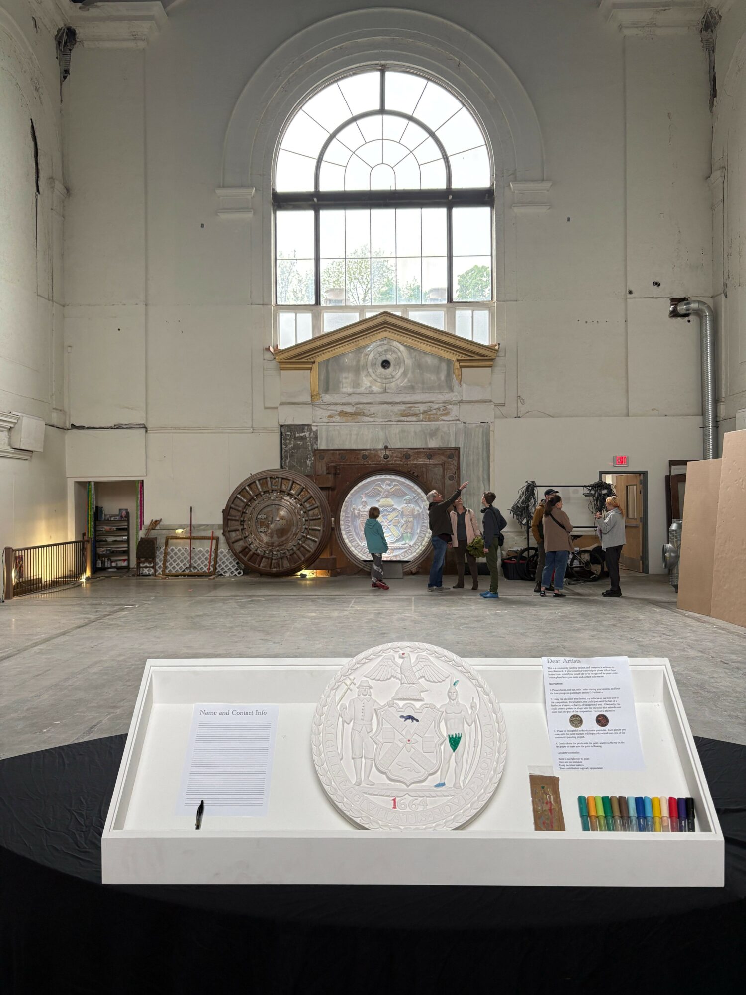Exhibition space with a large arched window, display table with artifacts, and a white informational stand.