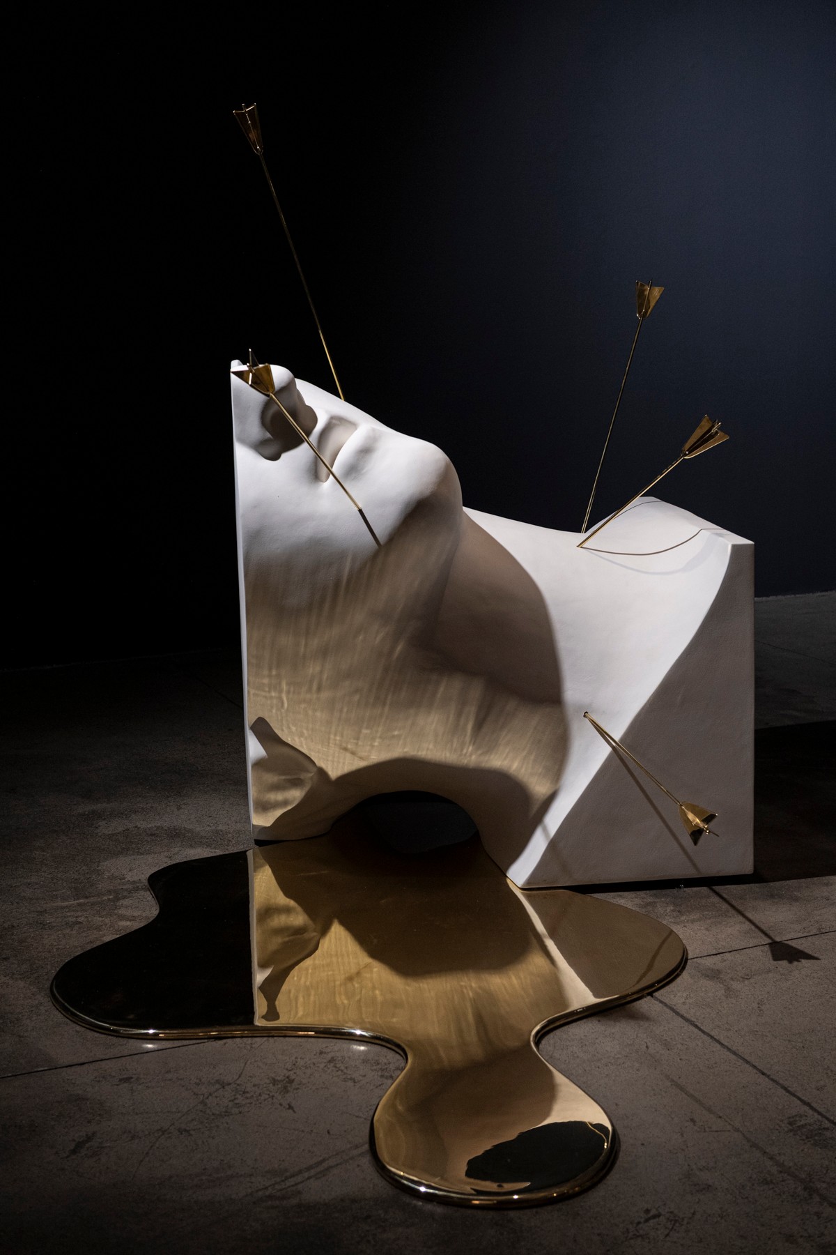 Reflective sculpture with arrows piercing a distorted, metallic surface, set against a dark background.