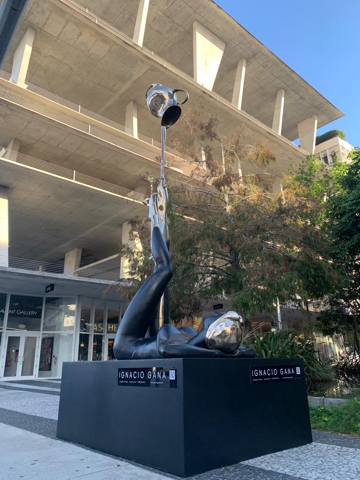 Modern building with a sculpture of a person reaching for a ball on a black pedestal, trees in the background, clear sky.