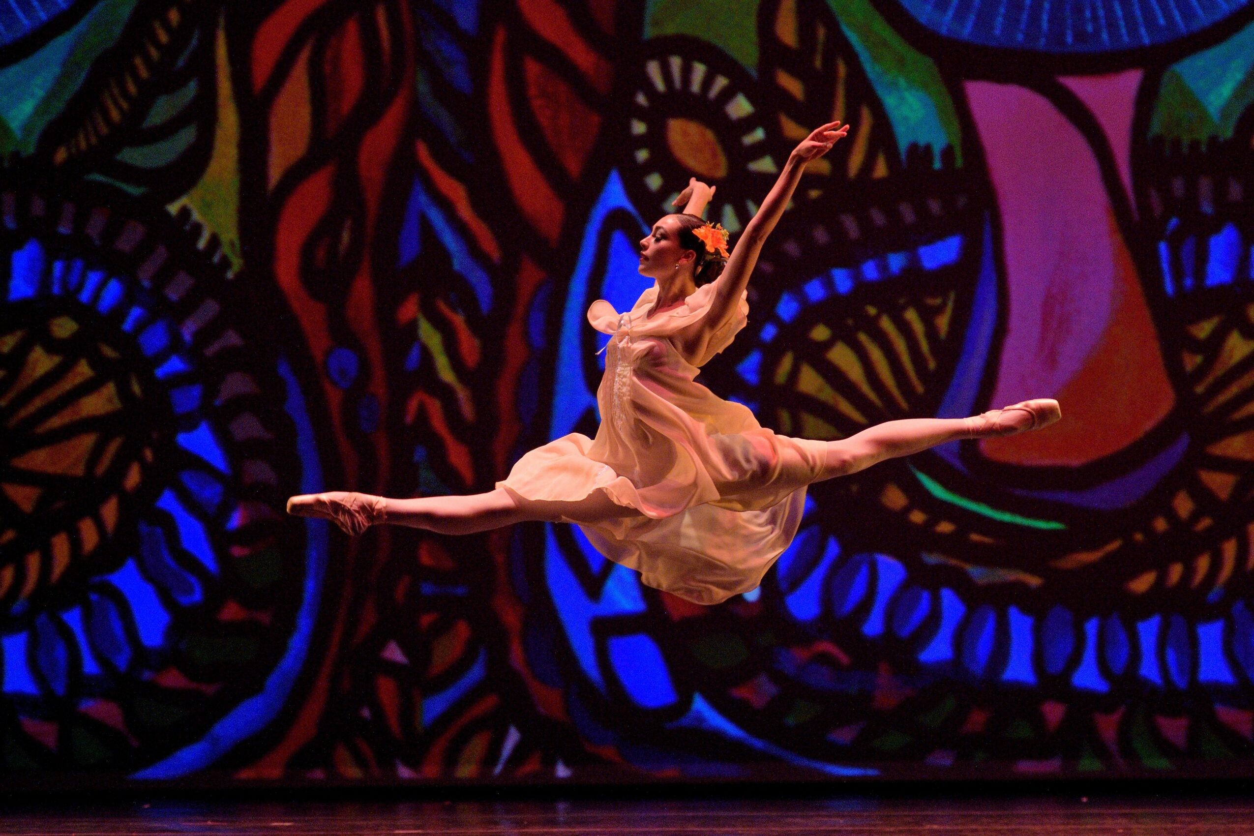 Ballet dancer performing a leap on stage with a colorful abstract background.