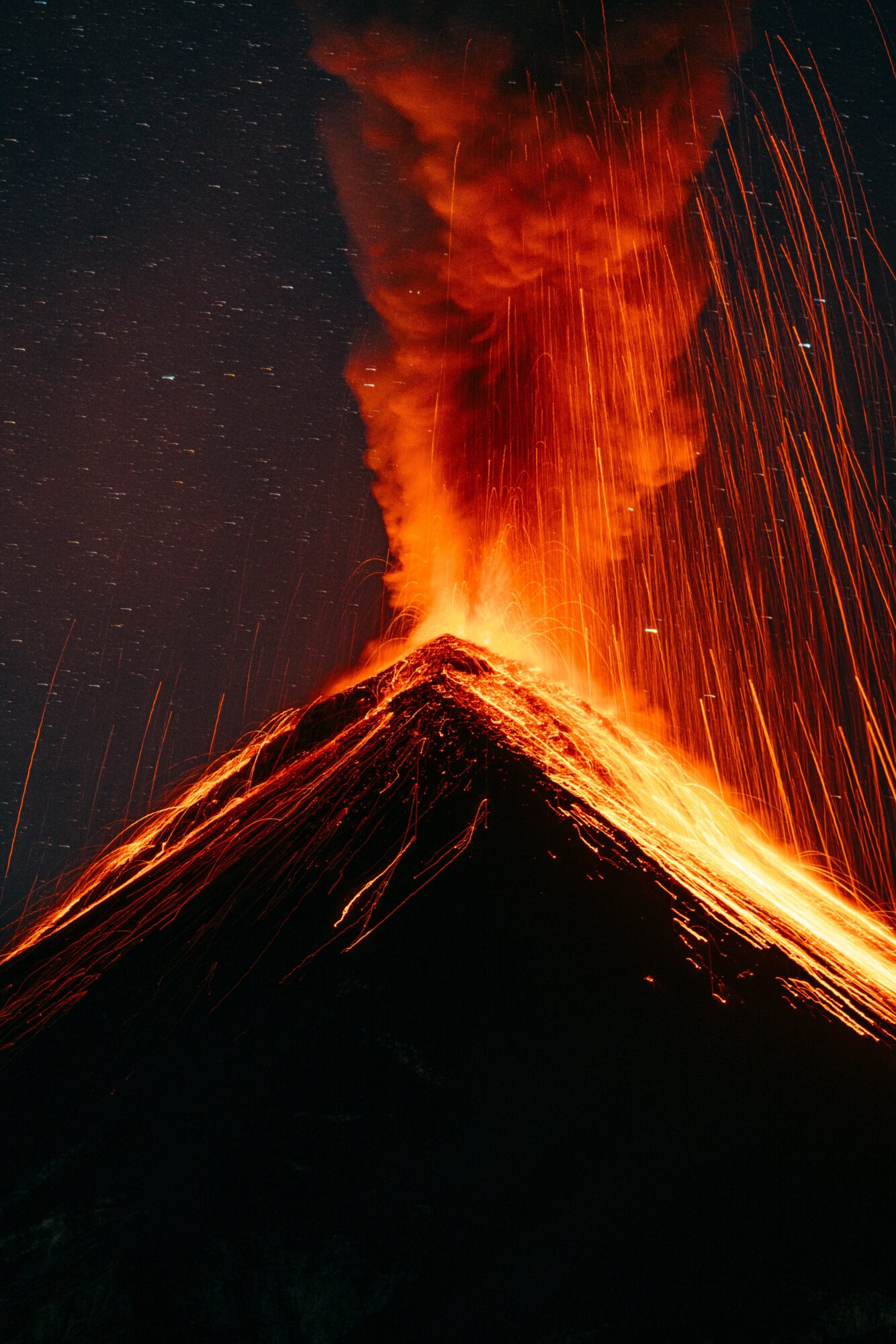 Erupting volcano spewing lava and ash into night sky with sparks flying, illuminated by volcanic glow.