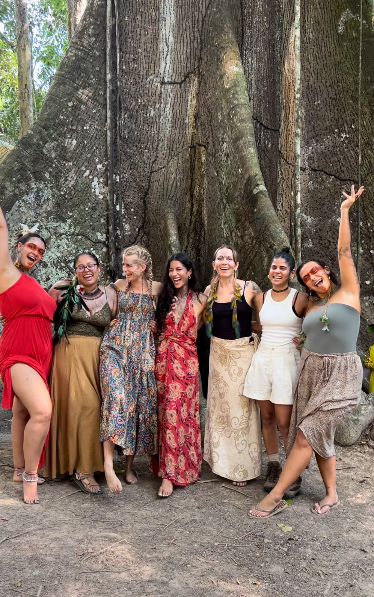 Seven women standing in front of a large tree, smiling and posing outdoors.