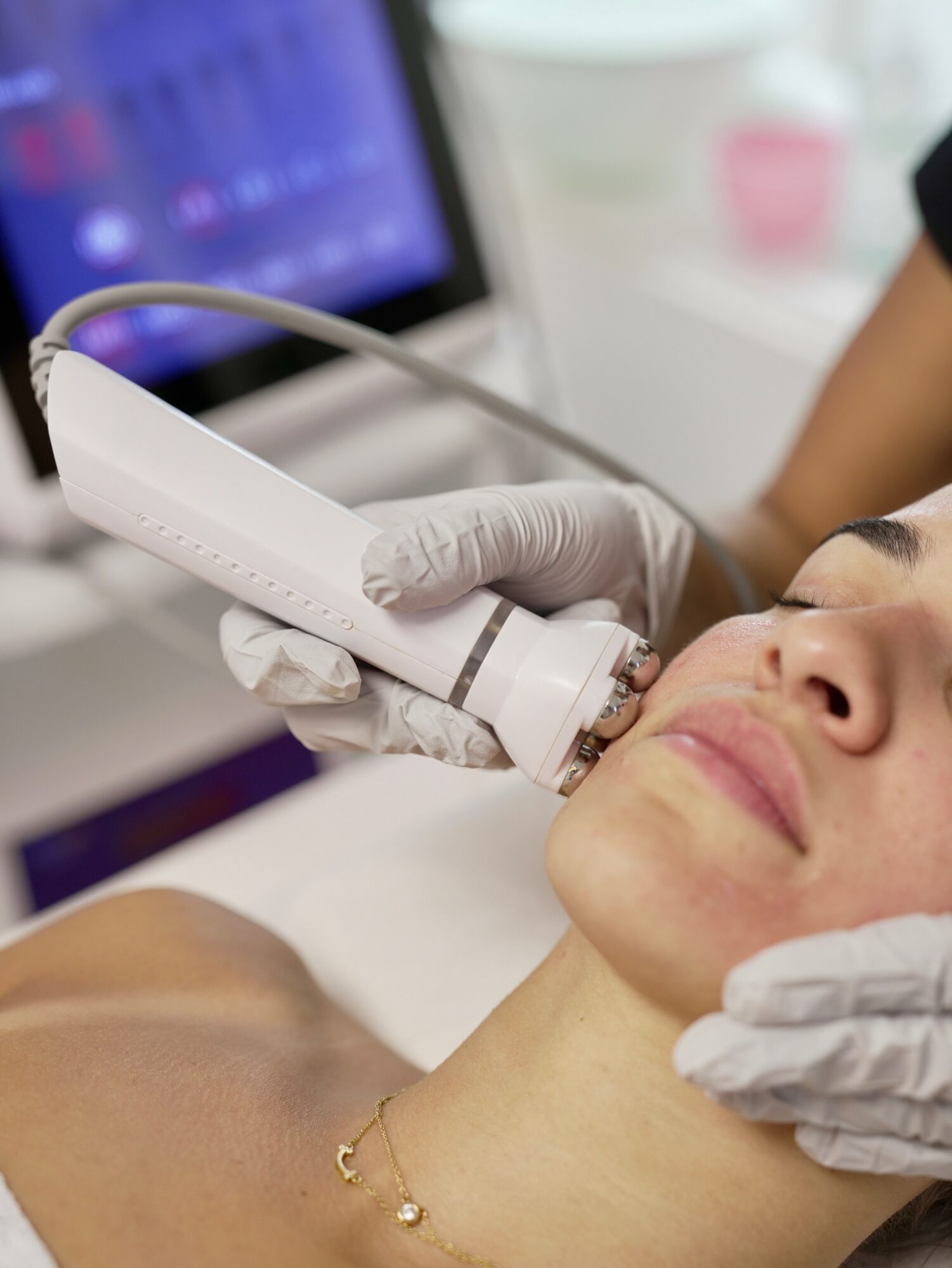 Medical professional performs an ultrasound on a woman's neck using a handheld device, with a monitor in the background.