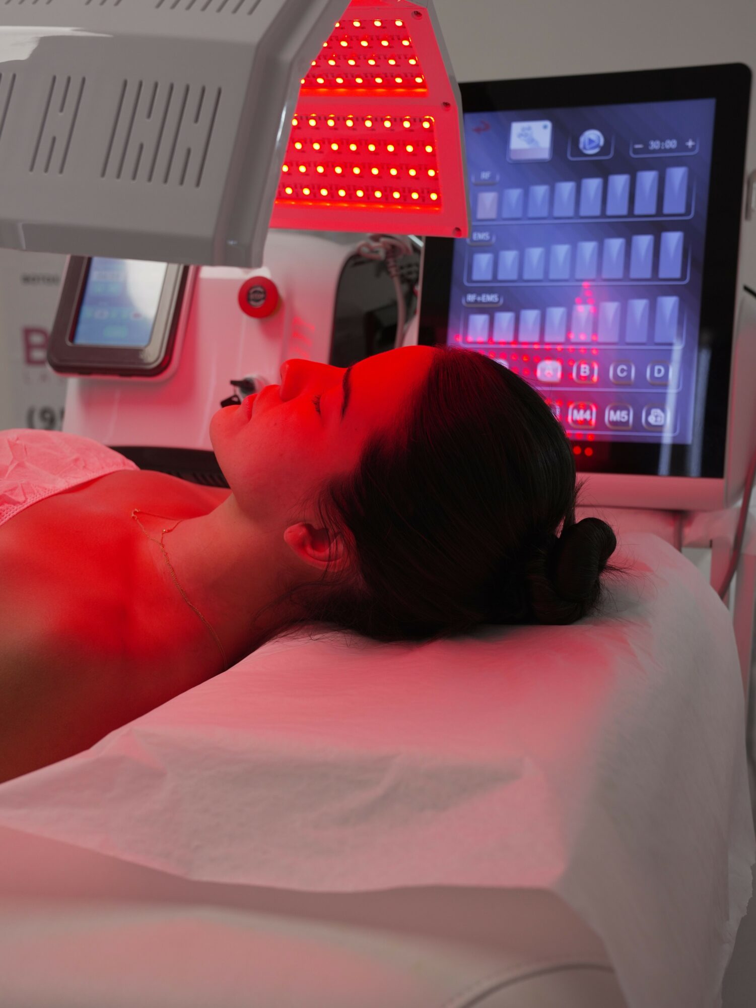 Person lying on medical bed with head turned to the side, surrounded by medical equipment and a screen displaying a grid.