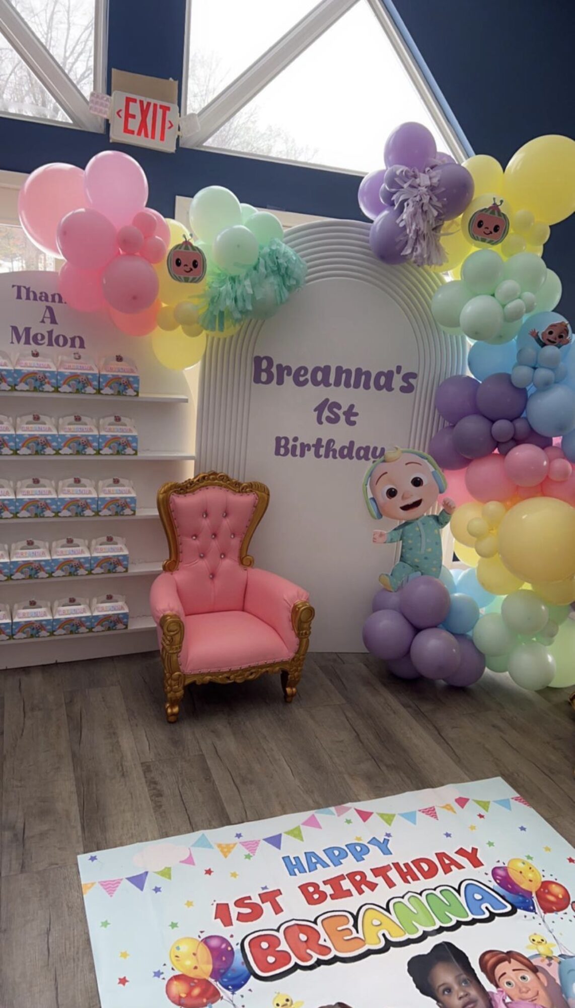 Pink armchair with gold trim in front of a birthday display with balloons and a sign reading 'Breanna's 1st Birthday'.