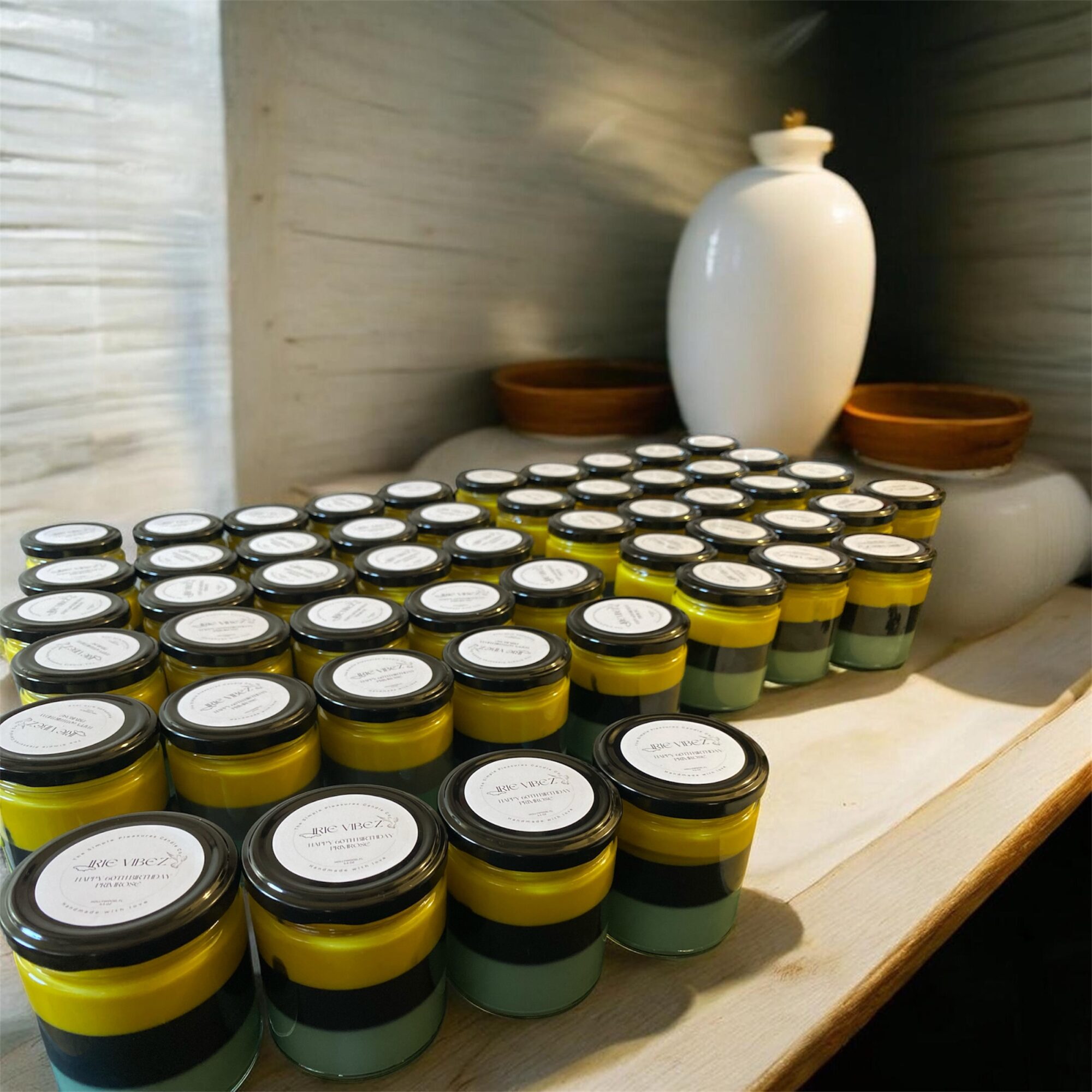 Multiple small jars with yellow, green, and black labels arranged on a wooden surface, with vases and bowls in the background.