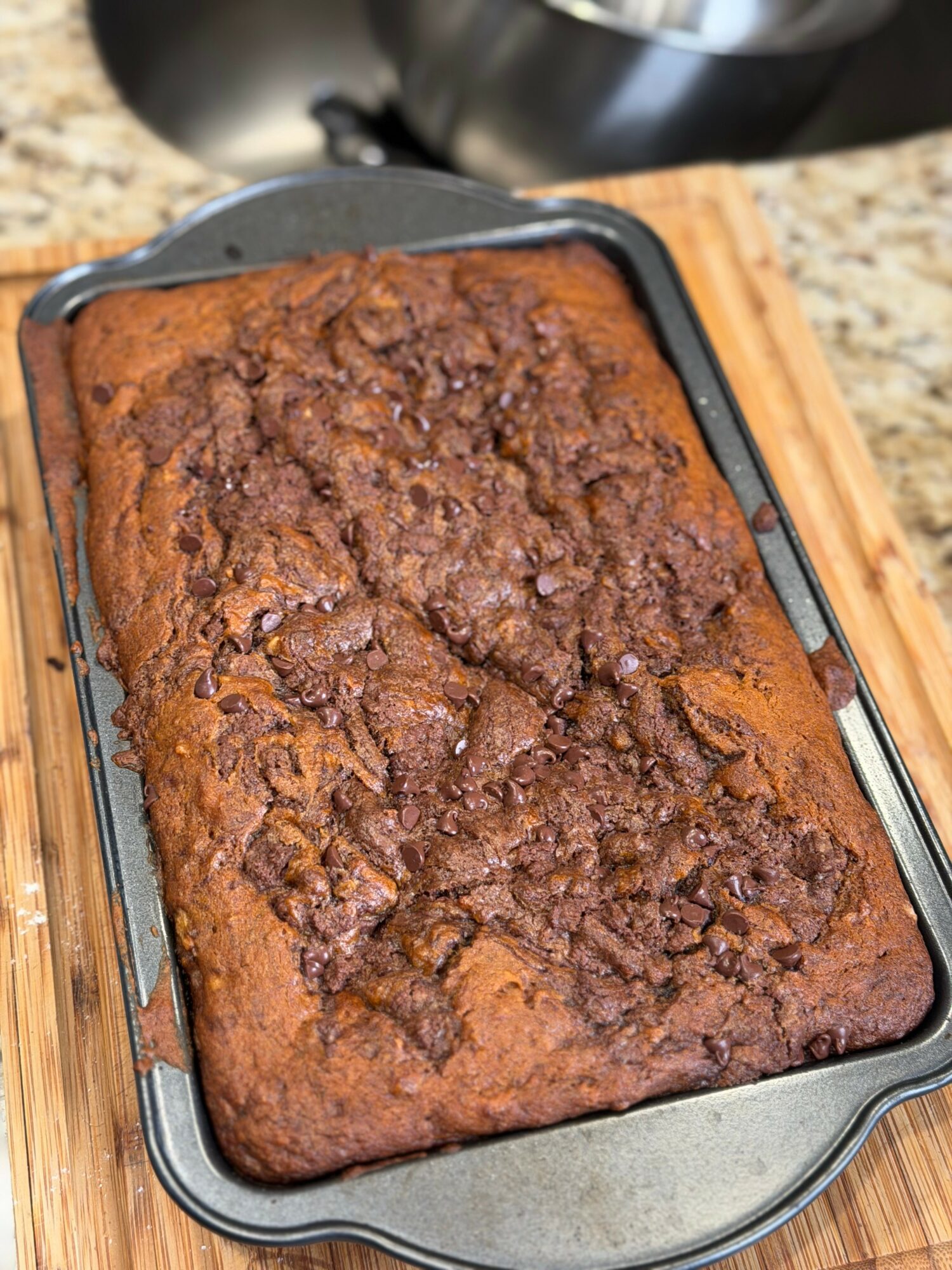 Baked rectangular loaf with a cracked, textured top in a metal baking pan on a wooden surface.