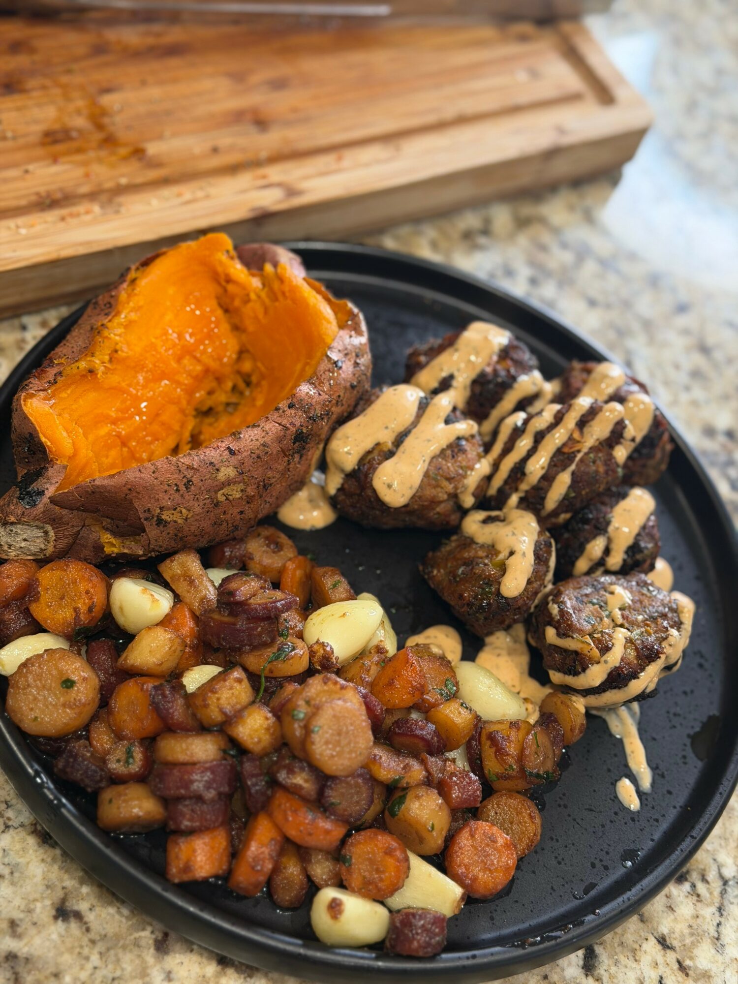 Sweet potato with toppings, cookies with drizzle, and a mix of roasted vegetables on a black plate.