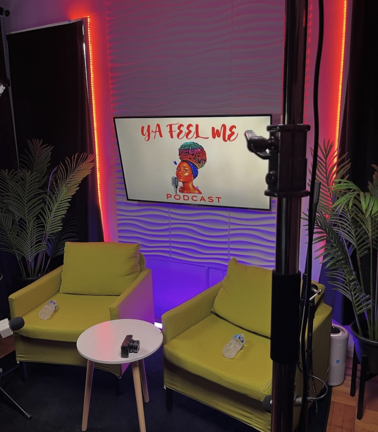 Podcast studio with two yellow chairs, a small white table, and a screen displaying 'U A FEEL ME PODCAST' with colorful graphics.