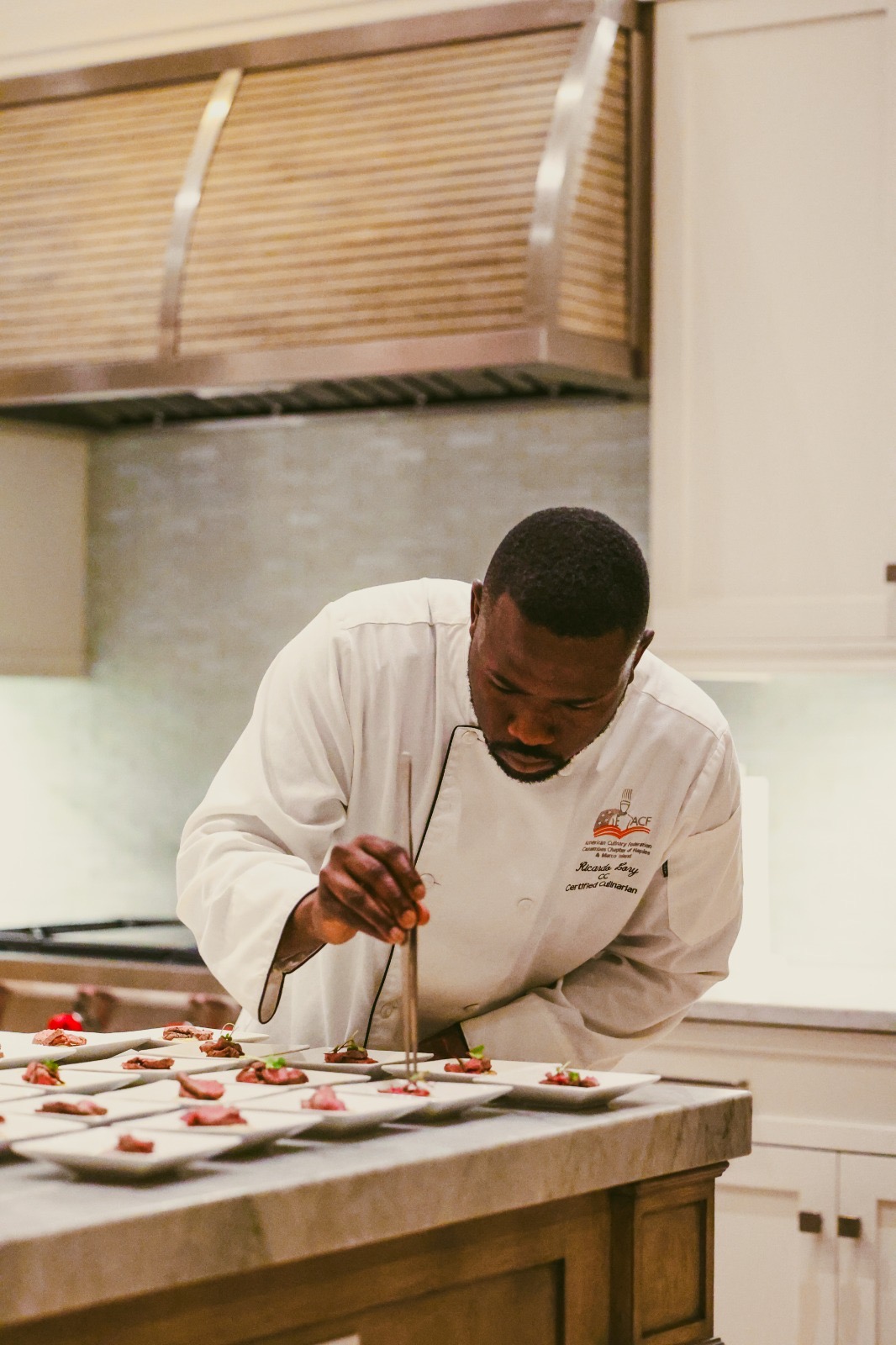 Chef in white coat decorating cookies on a kitchen counter, focused on work.