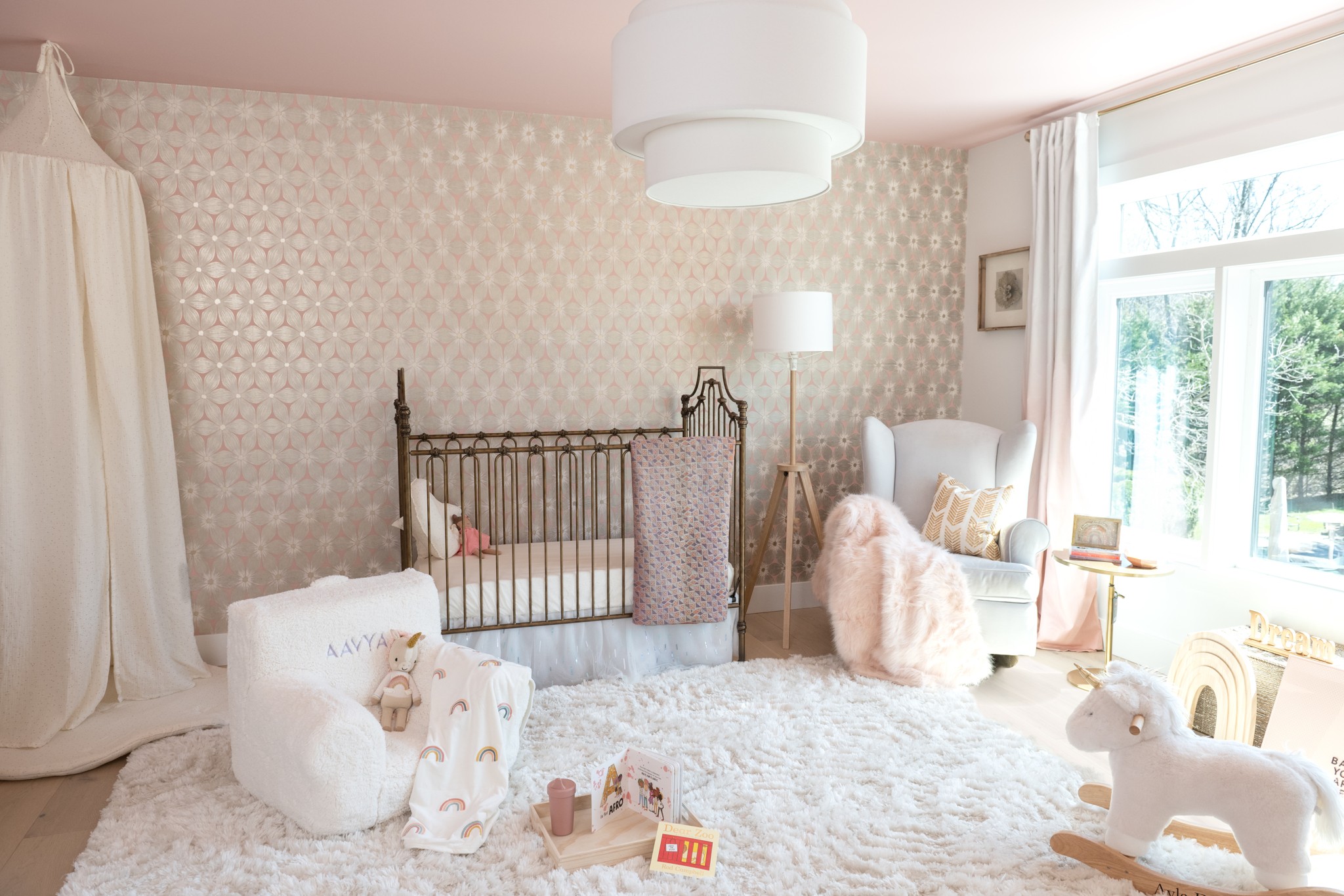Bright nursery with crib, armchair, and large window, decorated in soft pastel colors and plush toys, with a fluffy rug.