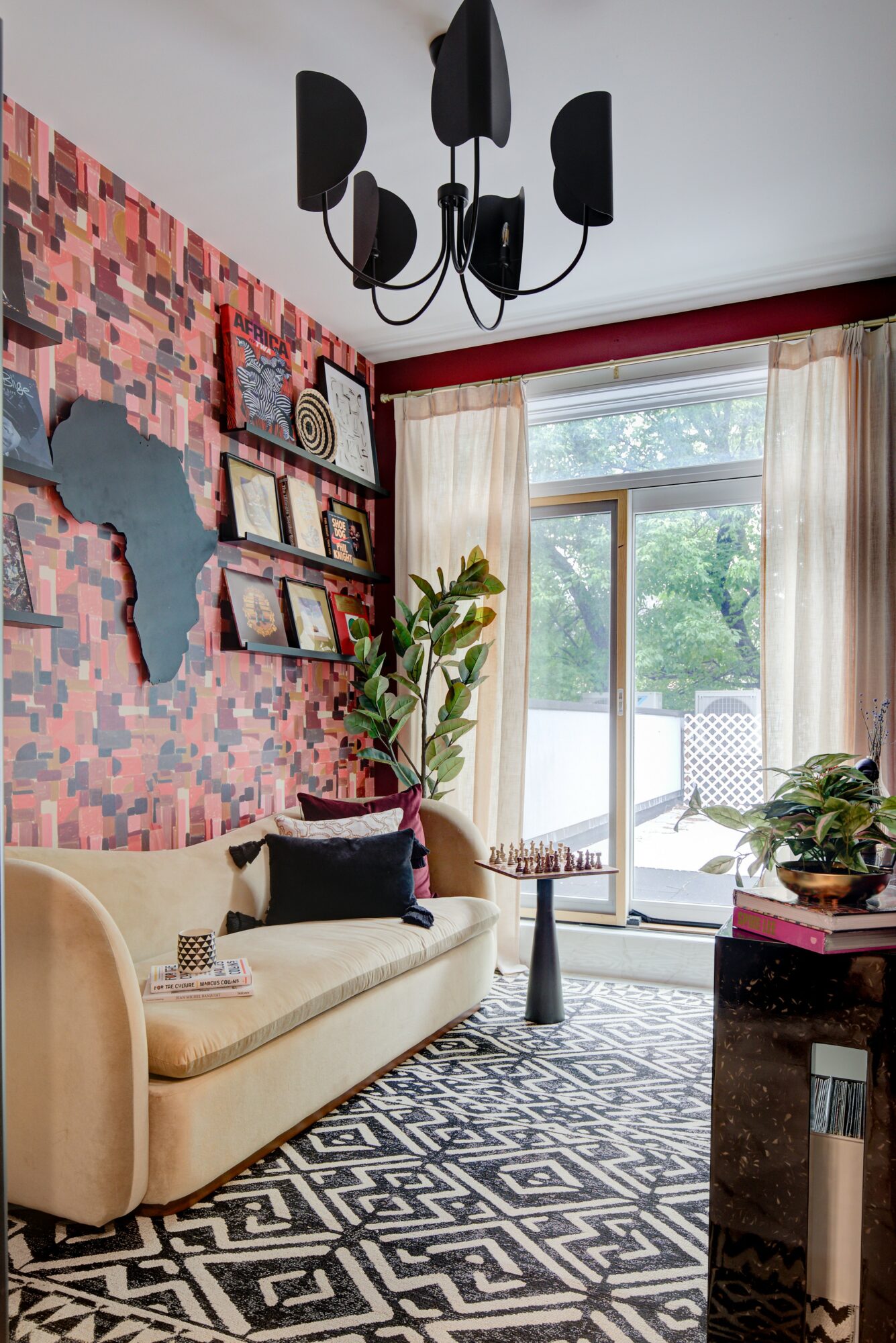Living room with beige sofa, colorful wall art, potted plant, window with curtains, and patterned rug.