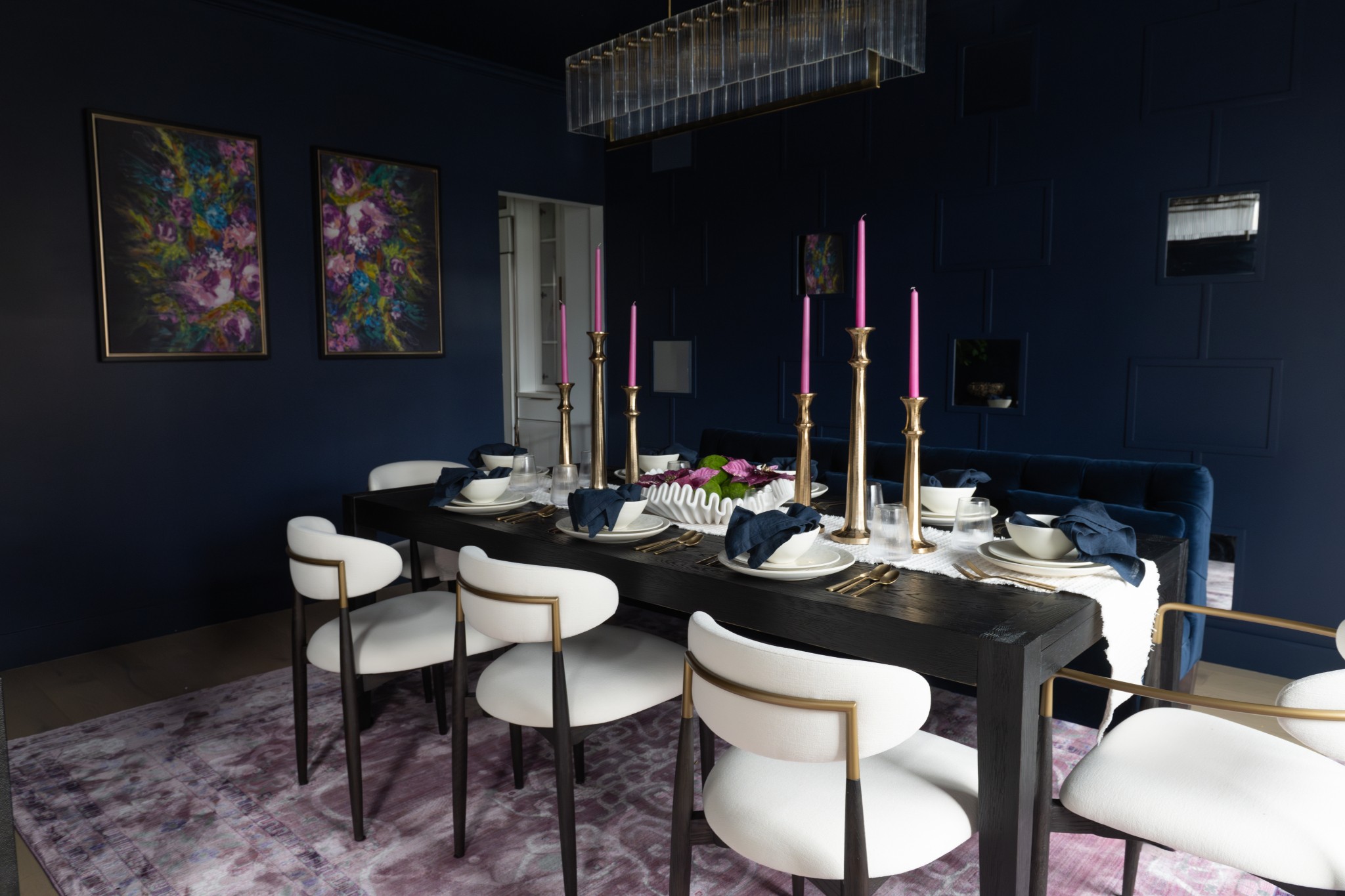 Dining room with a black table, white chairs, purple candles, and floral artwork on dark walls.