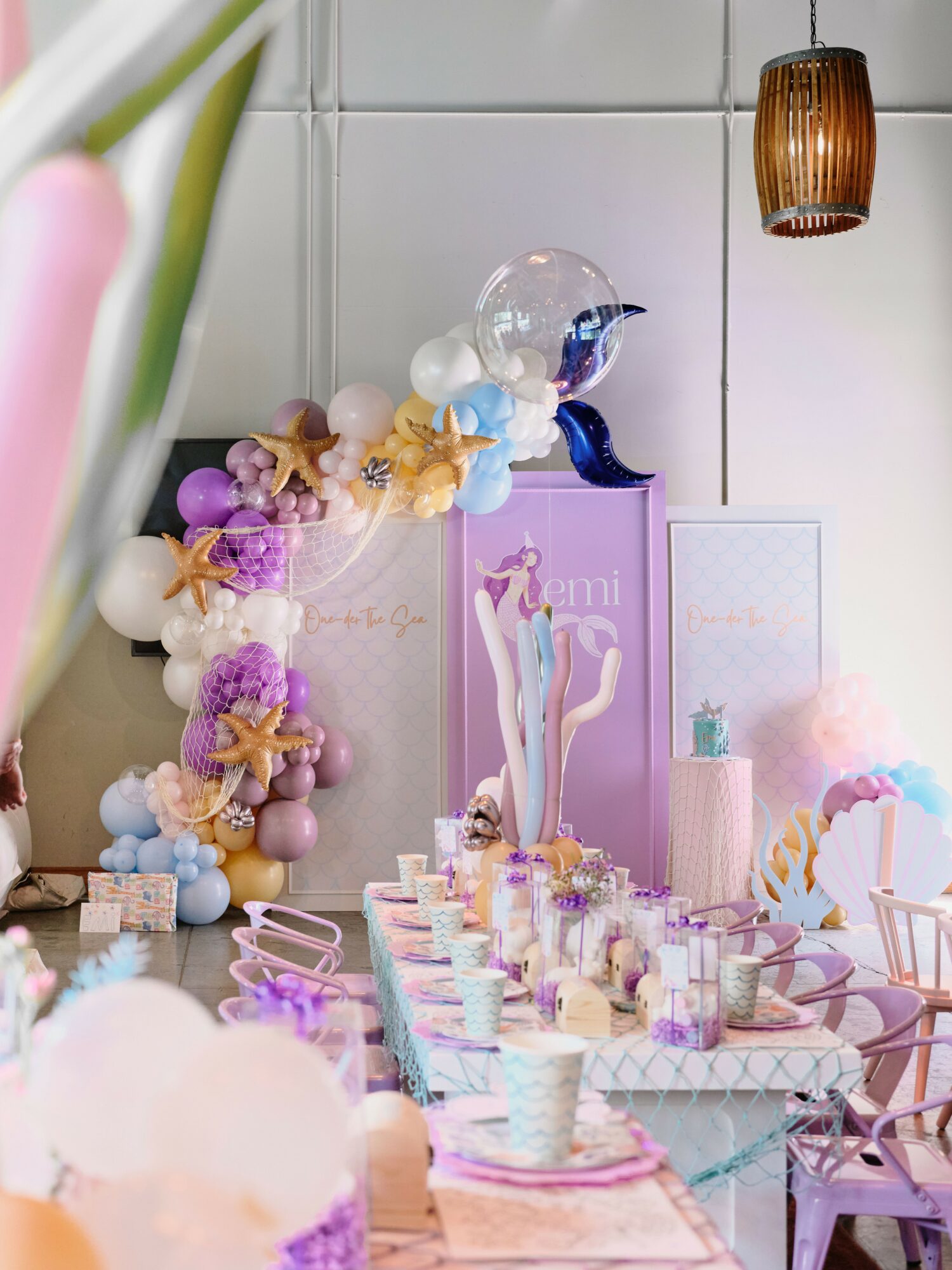 Decorative table with pastel balloons, flowers, and a unicorn figure, set for a celebration with cups and plates.