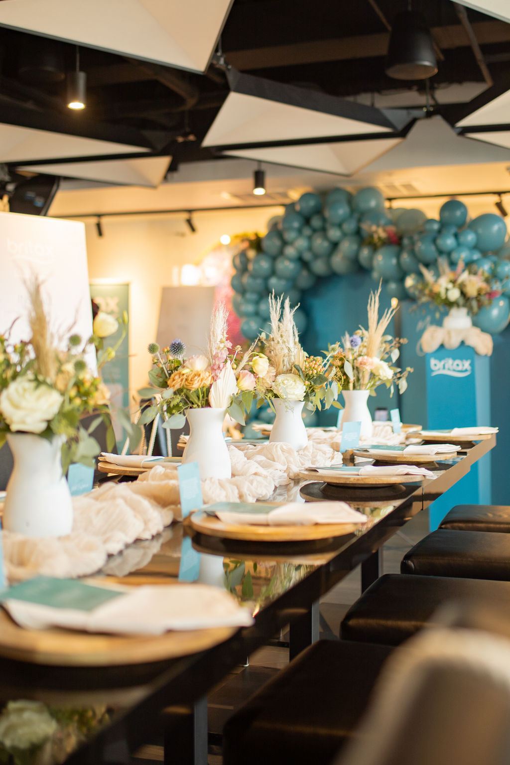 Table decorated with white vases, flowers, and balloons in the background, set for an event or celebration.