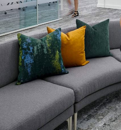 Gray sofa with three colorful pillows: green, yellow, and dark green, in a modern indoor setting.