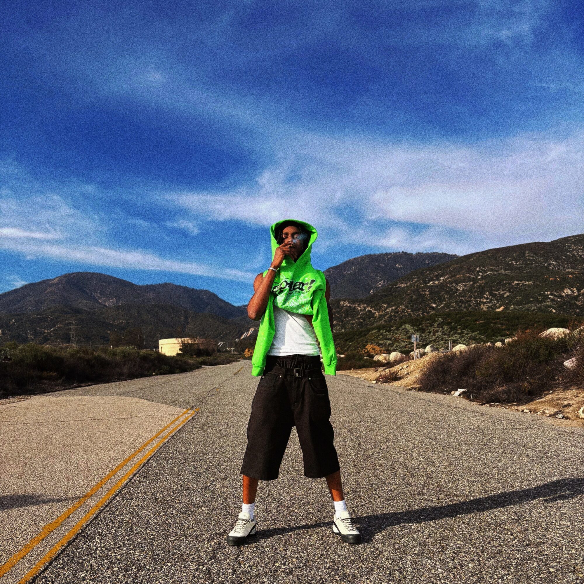 Person standing in the middle of a road with mountains and blue sky in the background.