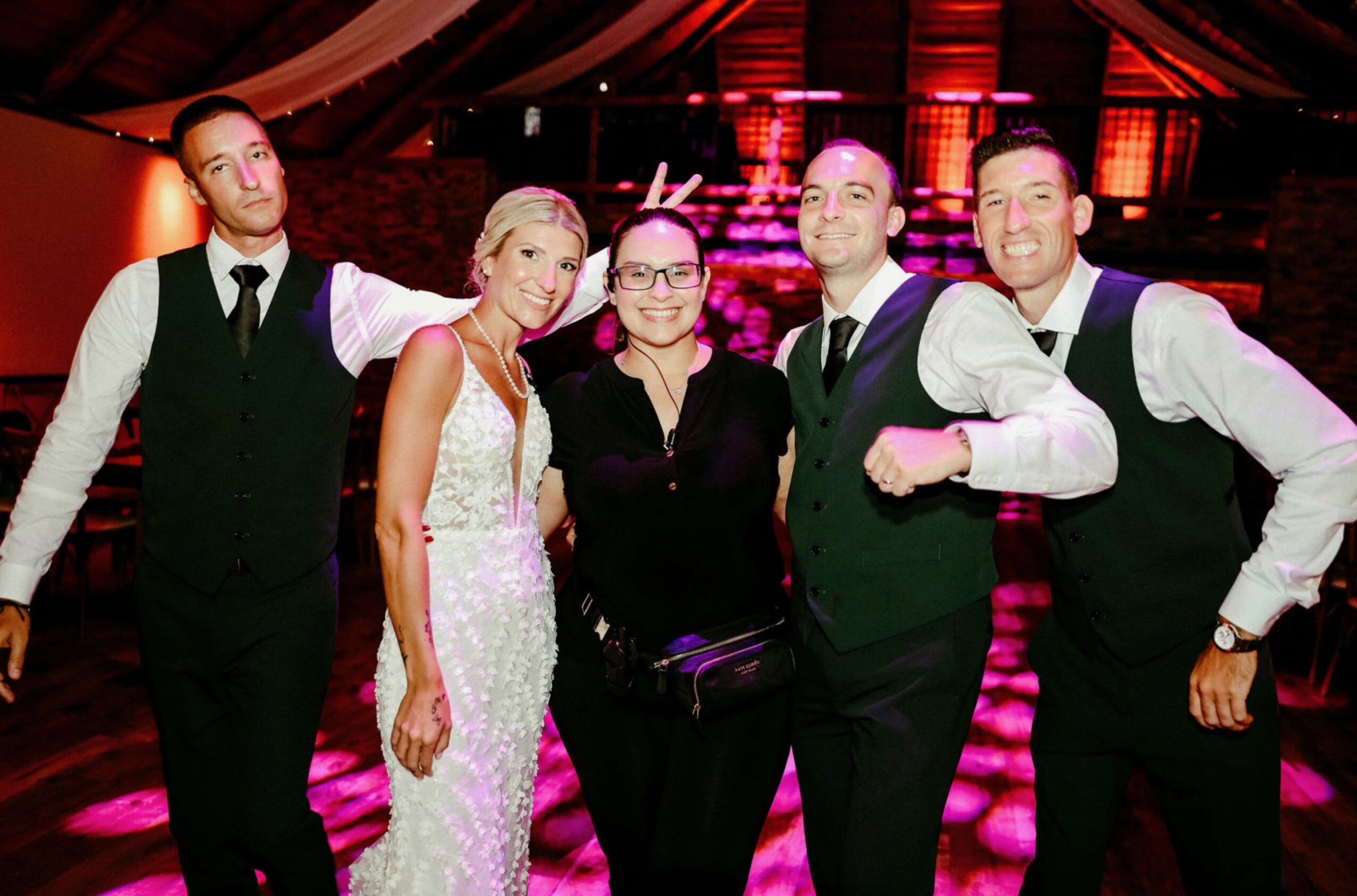 Group of six people dressed in formal attire posing indoors with colorful lighting, smiling at the camera.