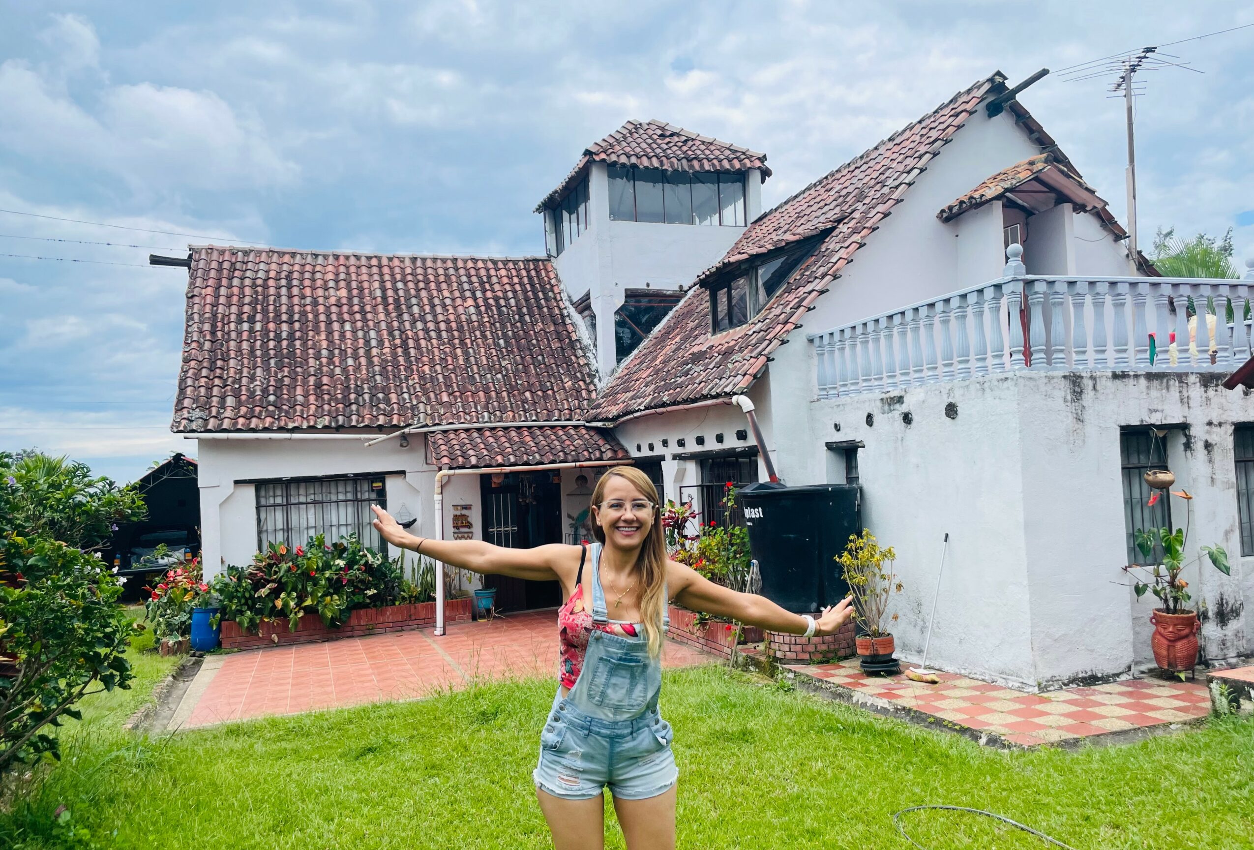 Young girl with arms outstretched standing in front of a white house with a red-tiled roof and green lawn.
