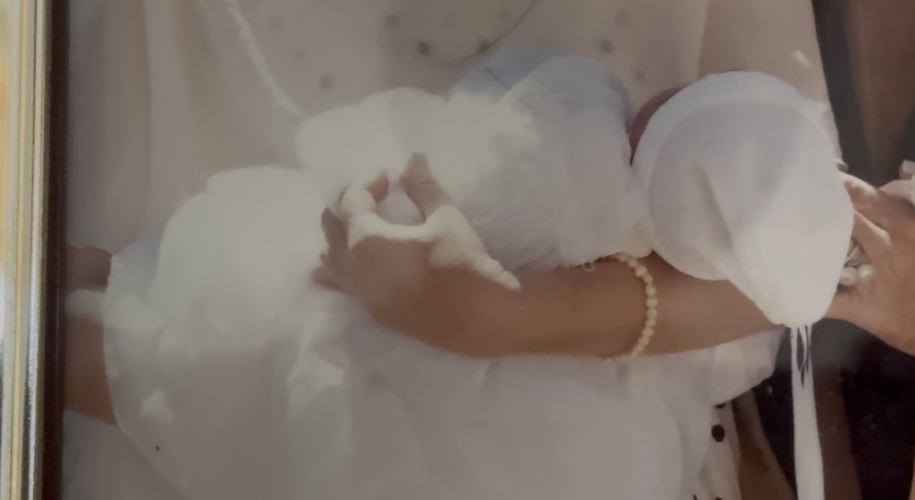 Person in white dress holding a bouquet, wearing a pearl bracelet, with a veil and lace details.