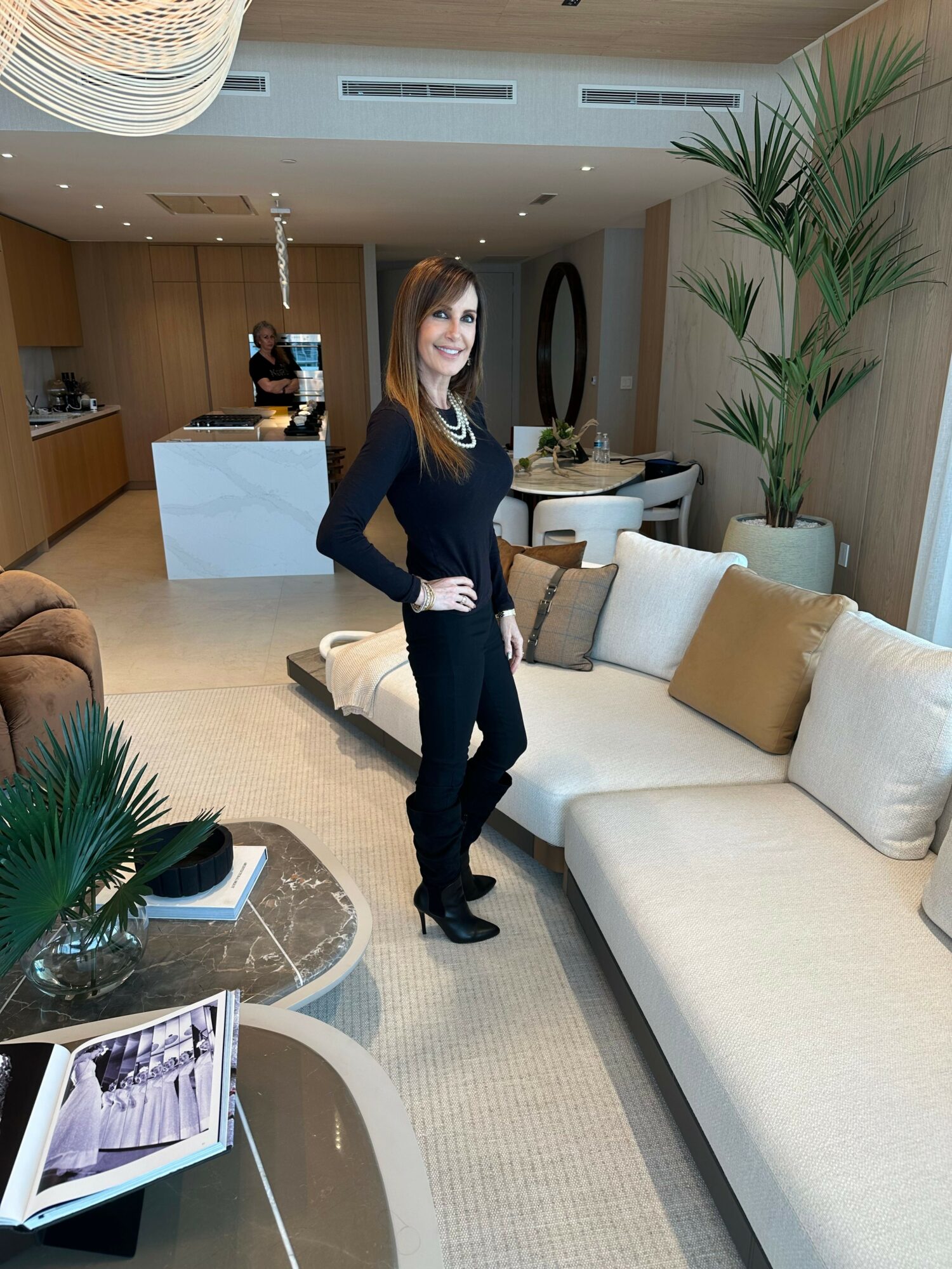 Woman standing in a modern living room with a white sofa, pillows, and a coffee table with a plant and magazine.