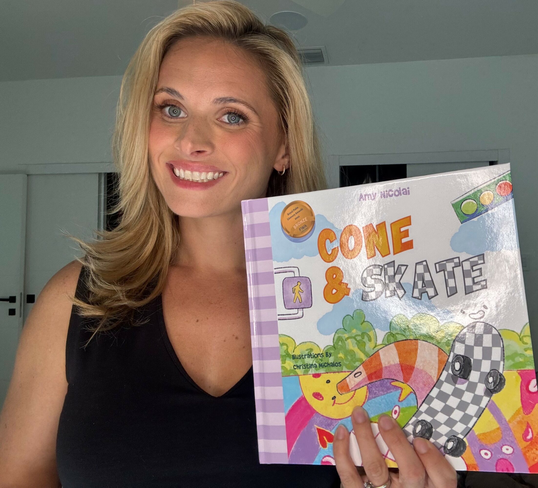 Woman with blonde hair smiling holding a colorful children's book titled 'Cone & Skate'.