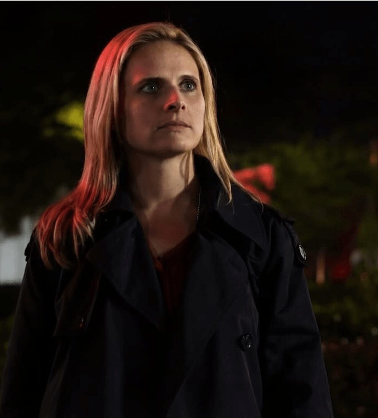 Woman with blonde hair wearing a dark jacket outdoors at night, looking to the side, illuminated by soft light.