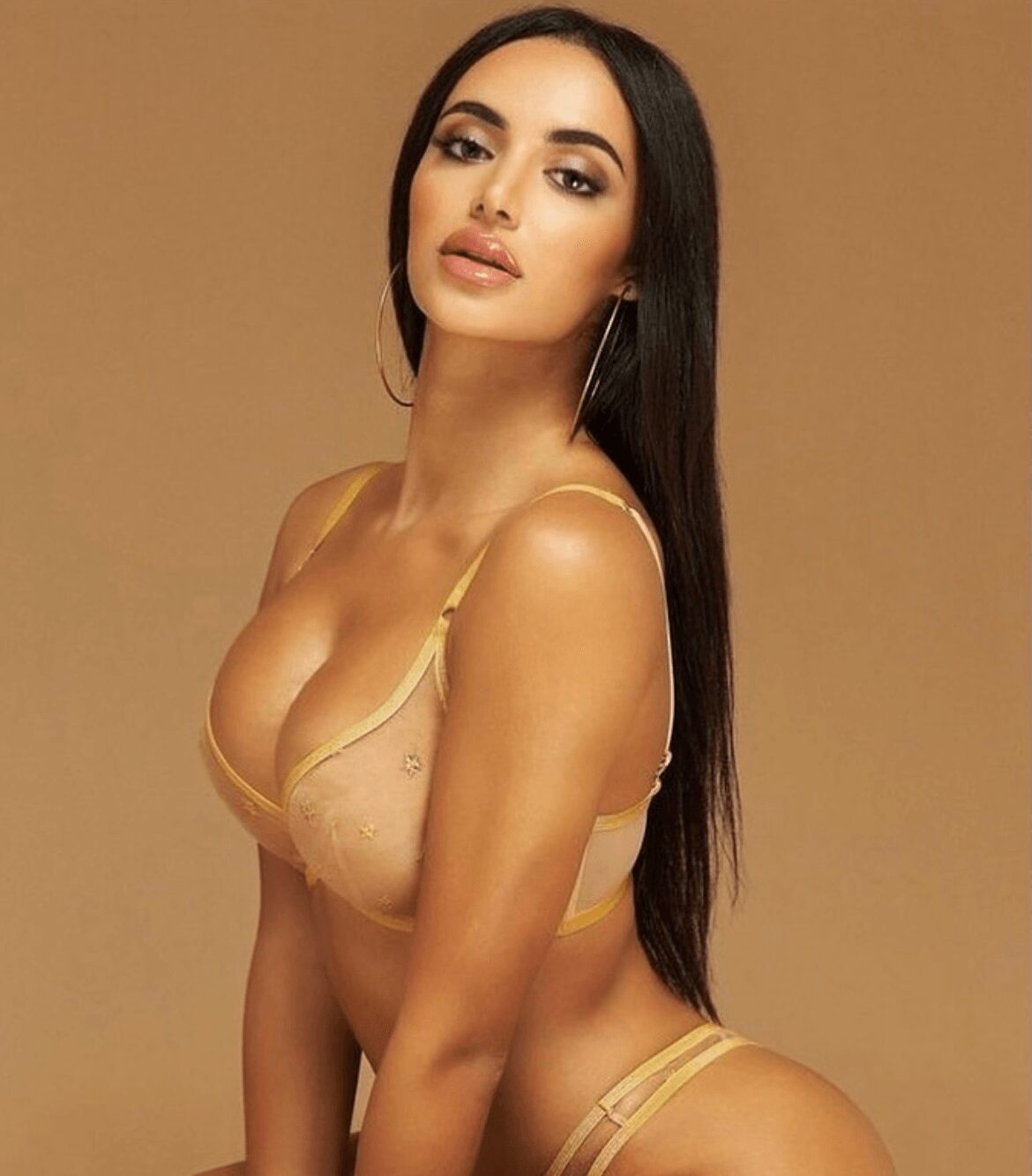 Woman with long dark hair in a yellow bra and matching underwear poses against a plain background.