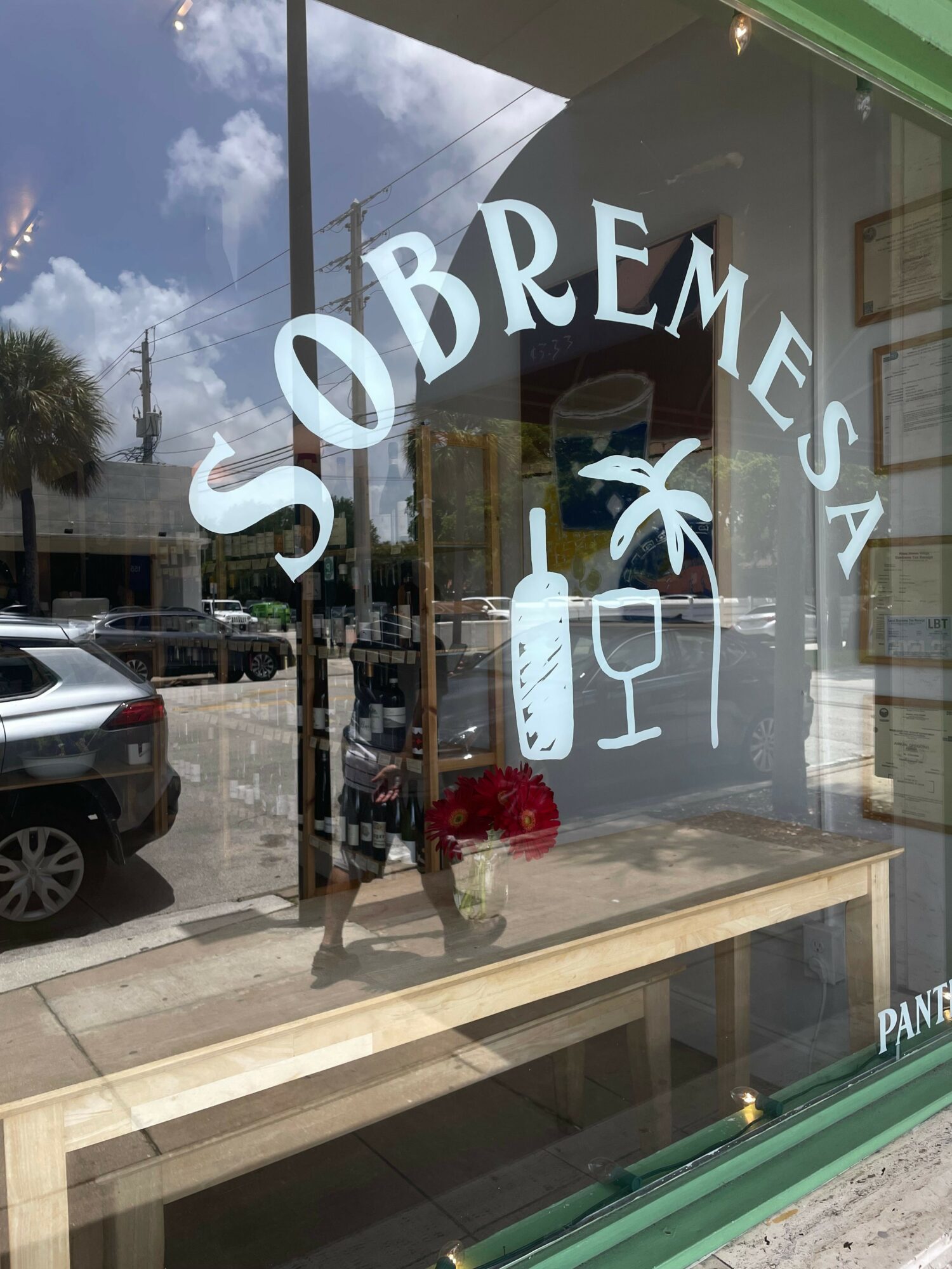 Storefront window with the word 'OBREMEZA' and a flower logo, reflecting the street scene outside.