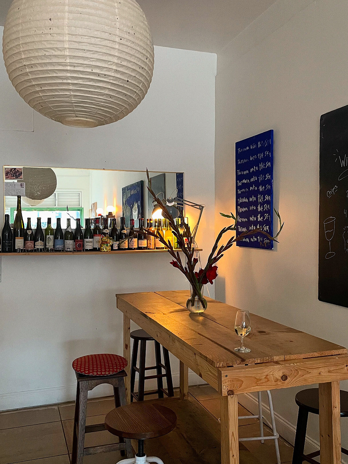 Interior of a cozy cafe with a wooden table, a vase with branches, a glass, and a bar with bottles in the background.