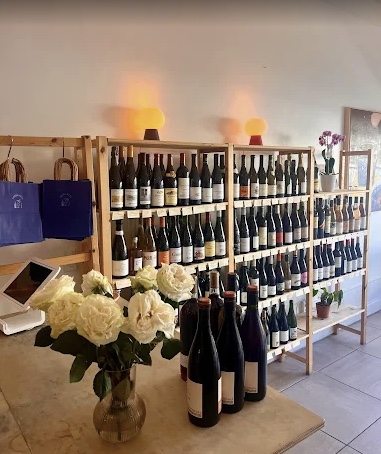 Shelves filled with wine bottles, a table with a vase of white flowers, and a wall with warm lighting. Word count: 20